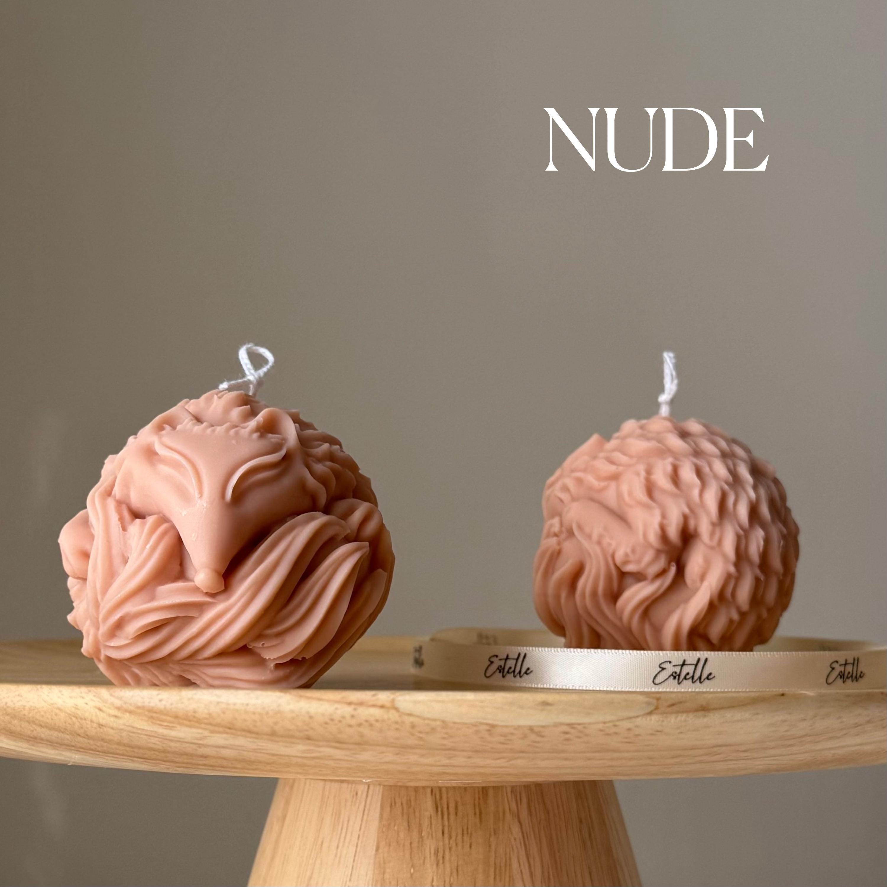 Two nude-colored candles shaped like abstract forms on a wooden stand with 'Estelle' branding.