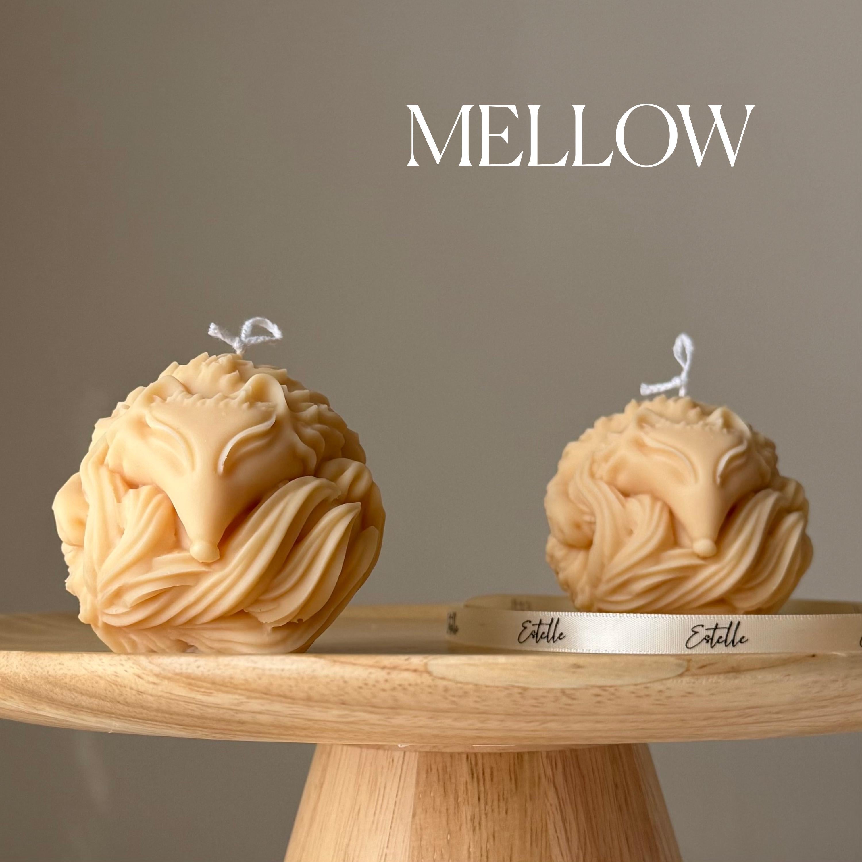Two fox-shaped candles on a wooden stand with 'Mellow' branding against a neutral background.