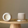 Two textured candles on a wooden stand with a neutral background