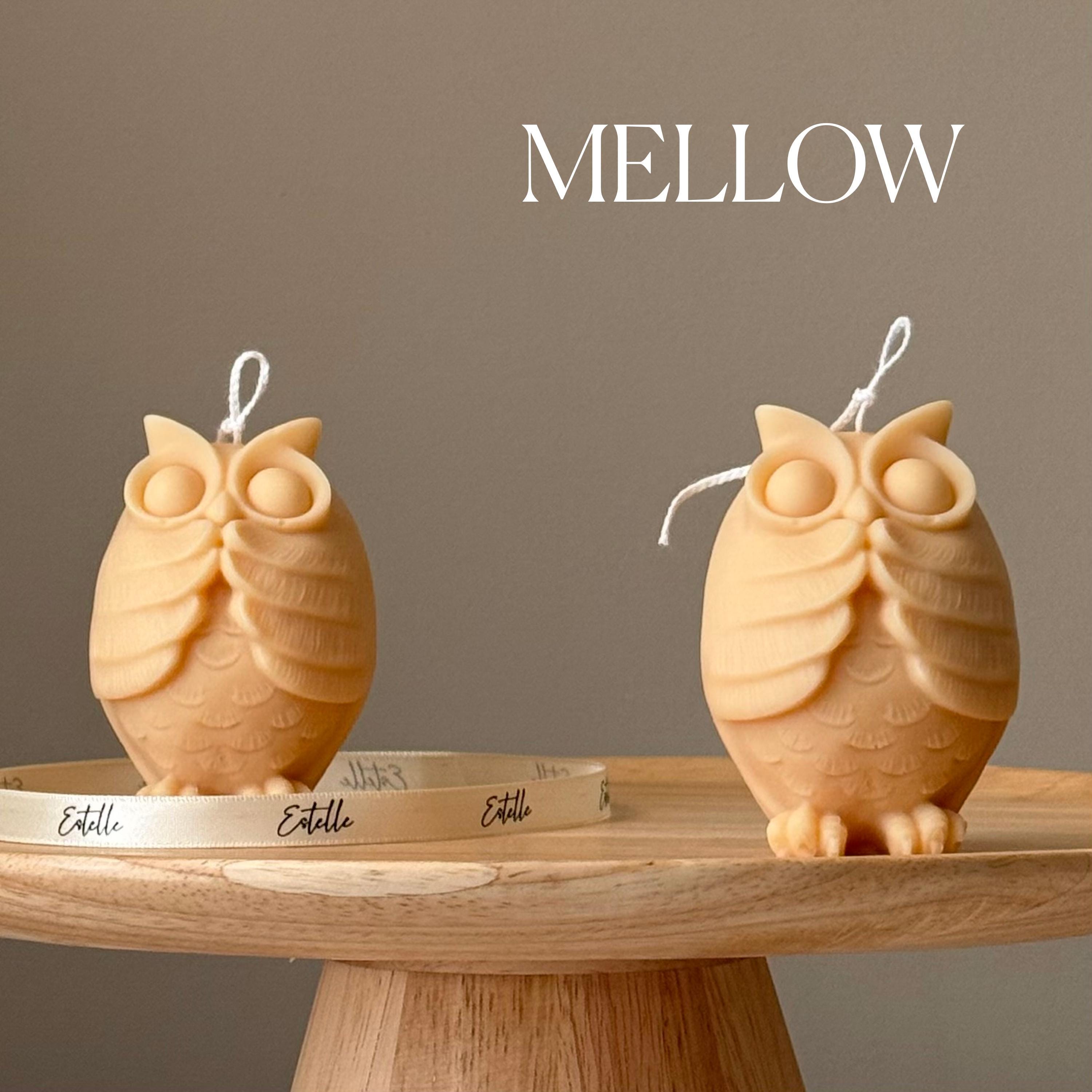 Two owl-shaped candles on a wooden stand with 'Mellow' branding above.