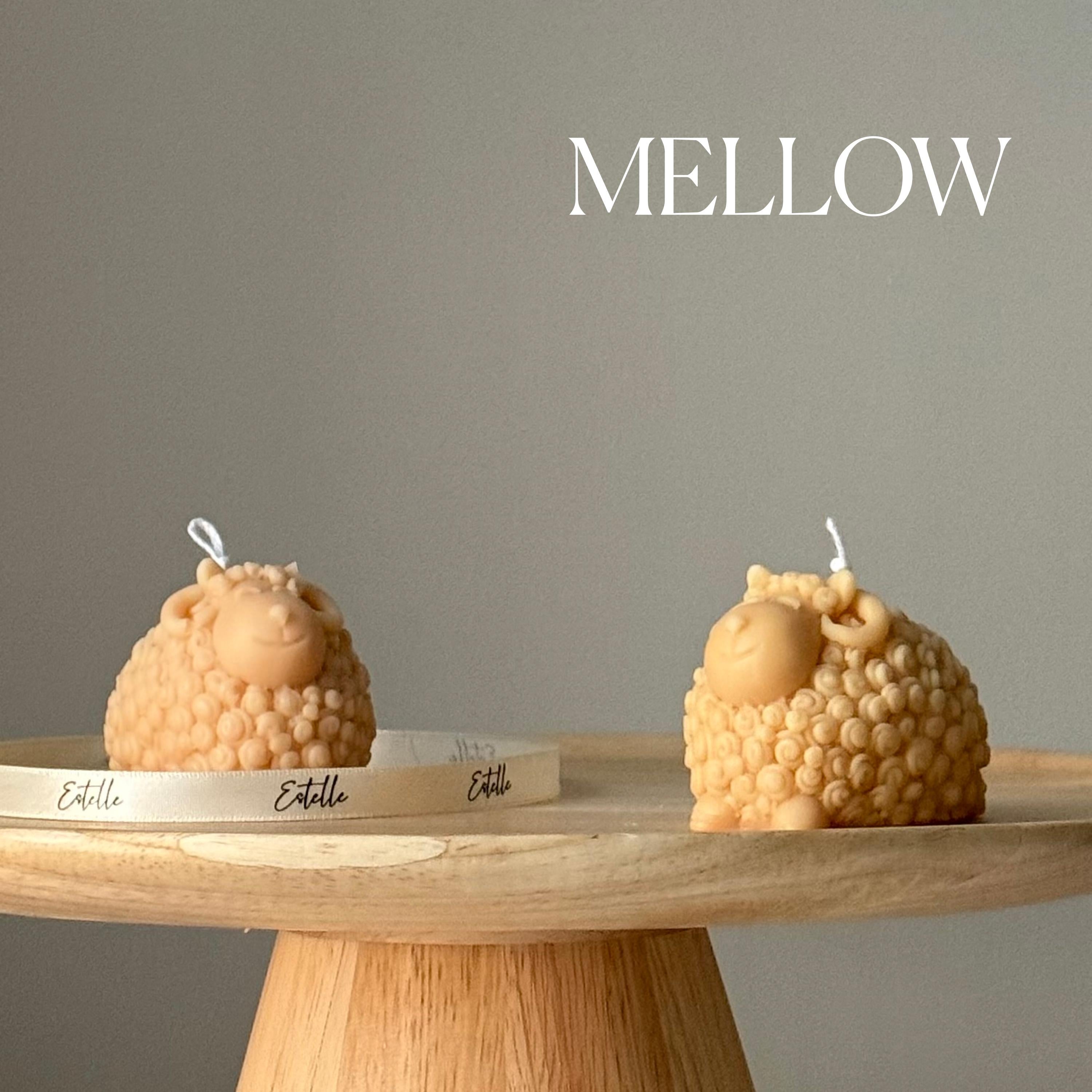 Two sheep-shaped candles on a wooden stand with 'Mellow' branding against a gray background.