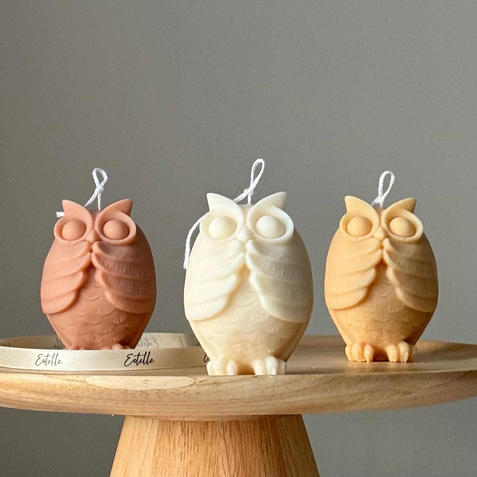 Three owl-shaped candles on a wooden stand with a neutral background