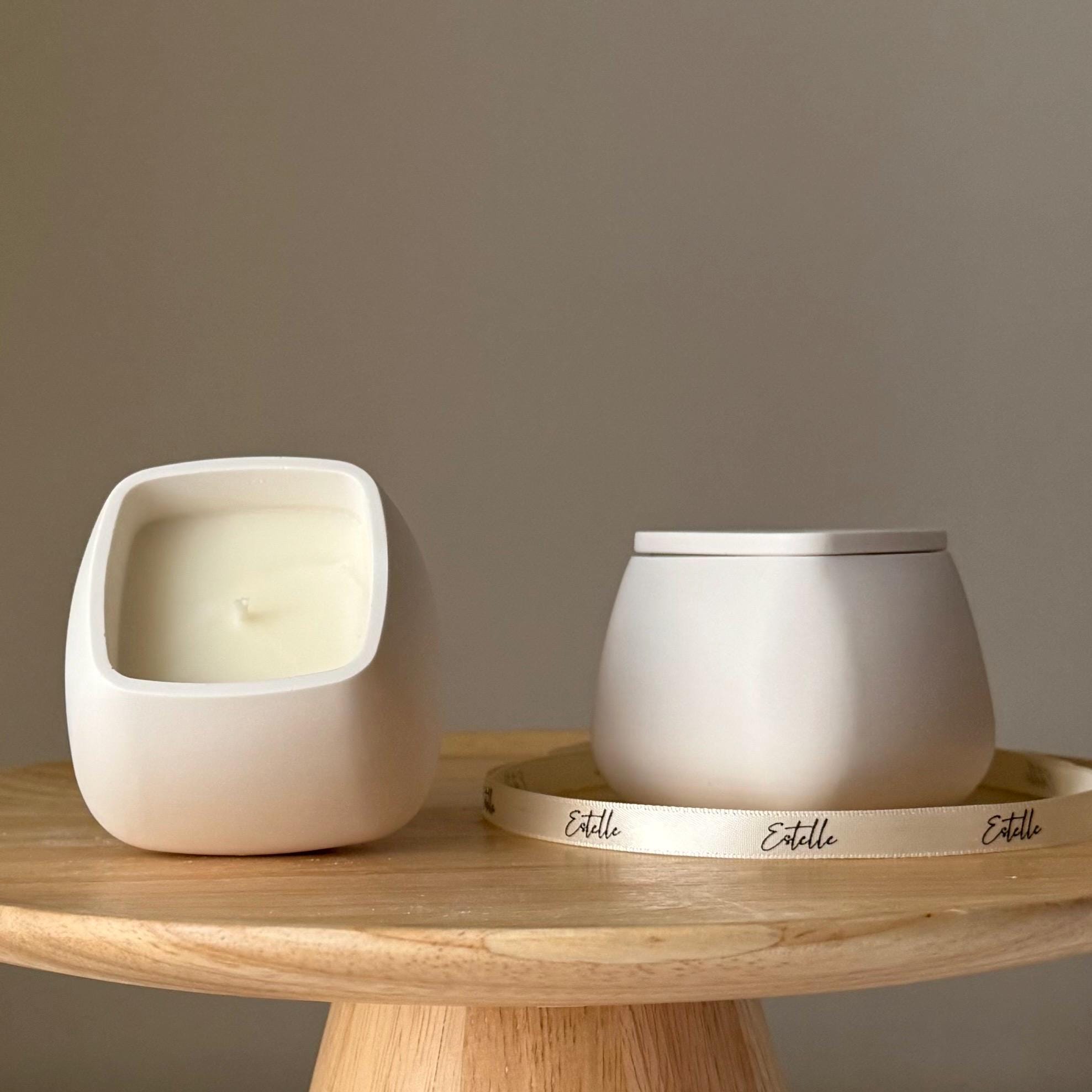 Two ceramic containers with a candle on a wooden table against a plain background