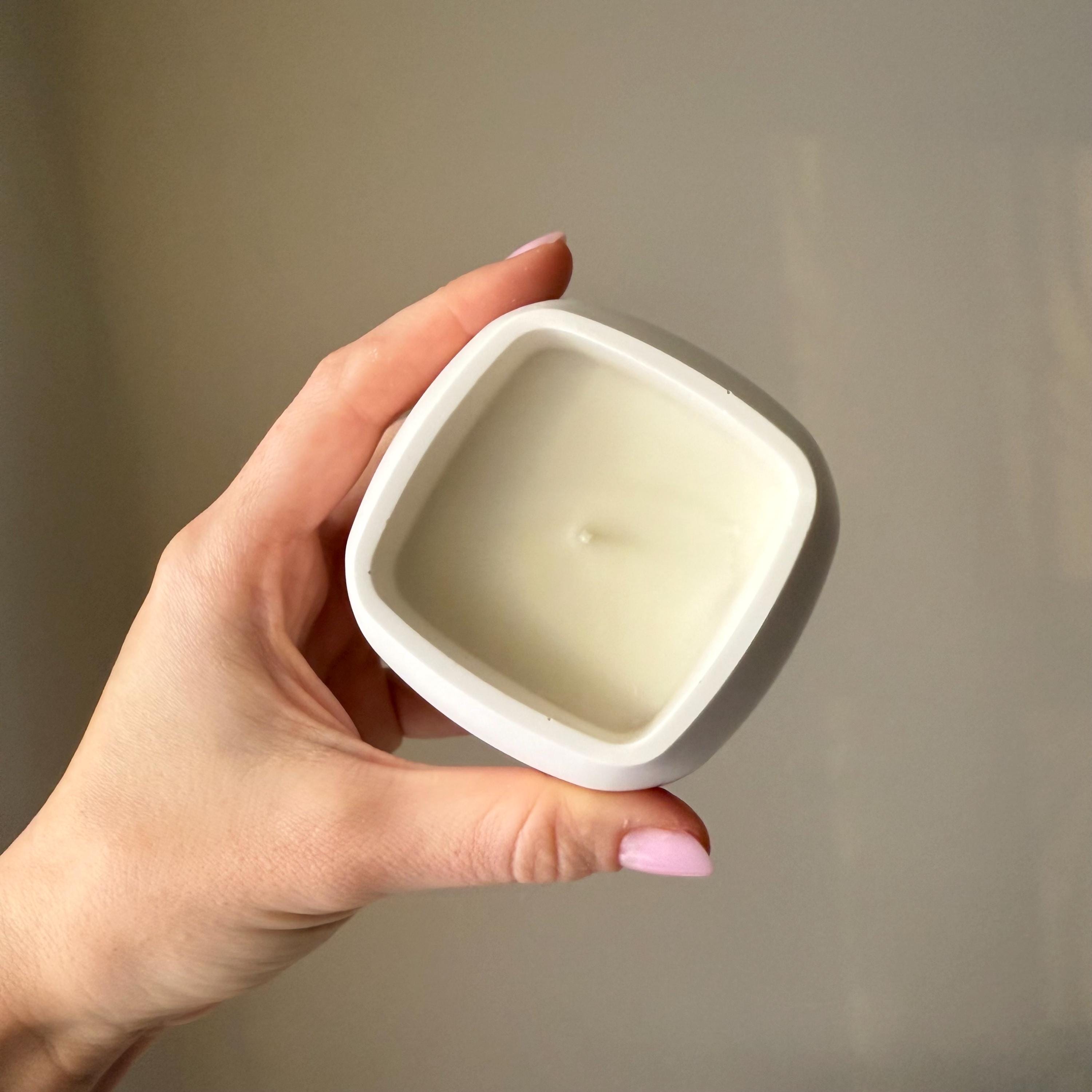 Hand holding a small square candle with a plain background