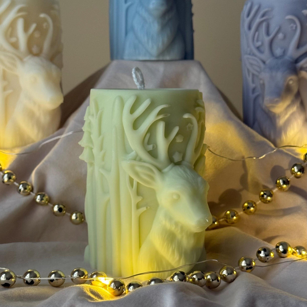 Mint green Decorative candle with deer design on a soft fabric background with gold beads.