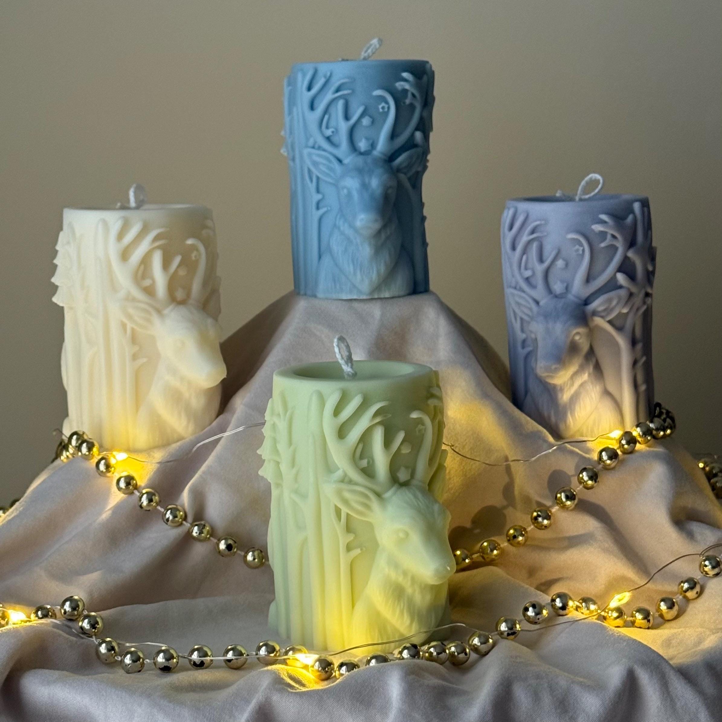 Decorative candles with deer designs on a fabric surface with string lights.