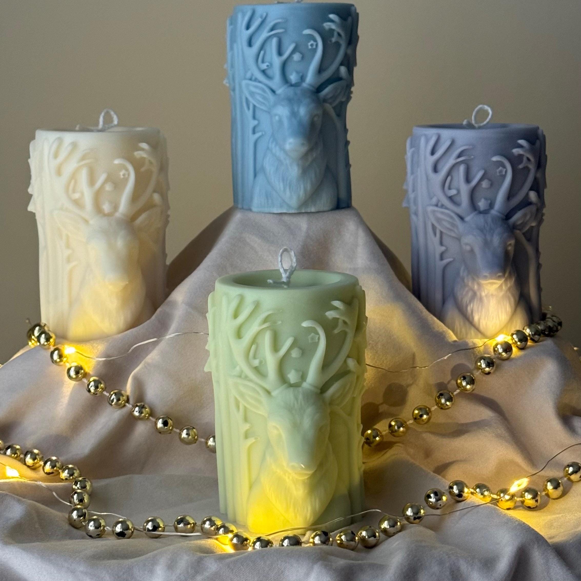 Decorative candles with deer head designs on a soft surface with string lights.