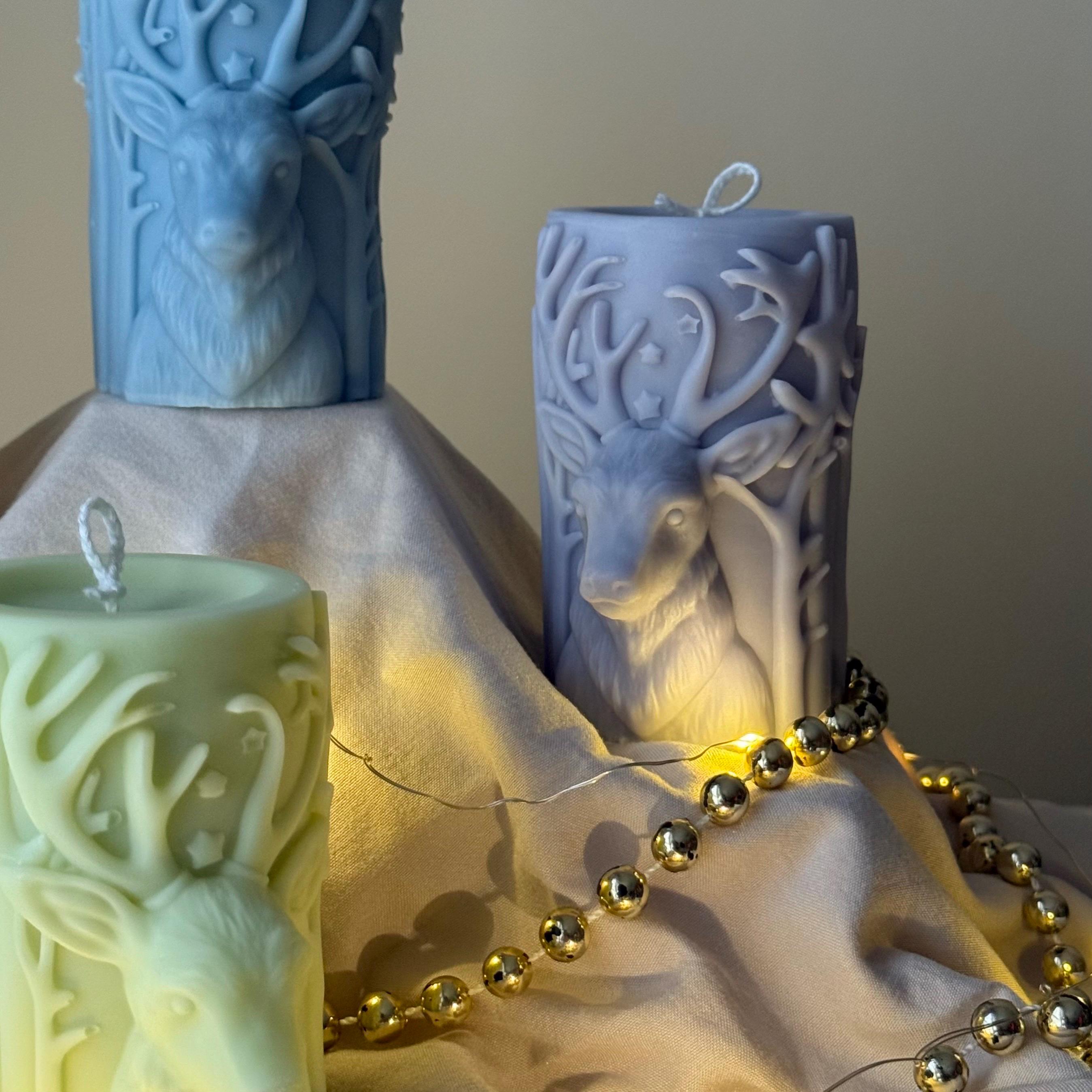 Lilac candles with deer designs on a fabric surface with a string of beads.
