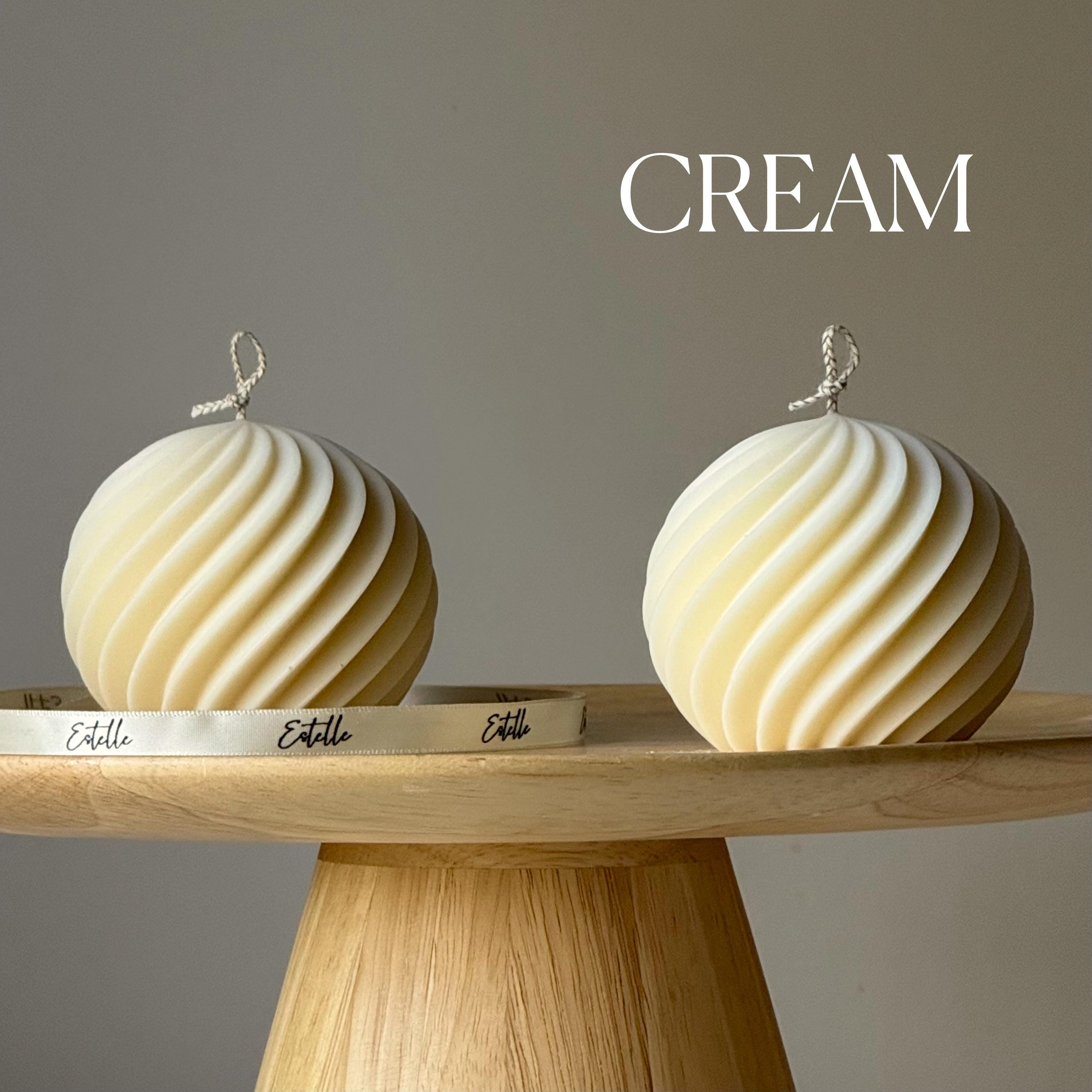 Two cream-colored spherical objects on a wooden stand with 'Estelle' branding, against a gray background.