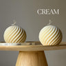 Two cream-colored spherical objects on a wooden stand with 'Estelle' branding, against a gray background.