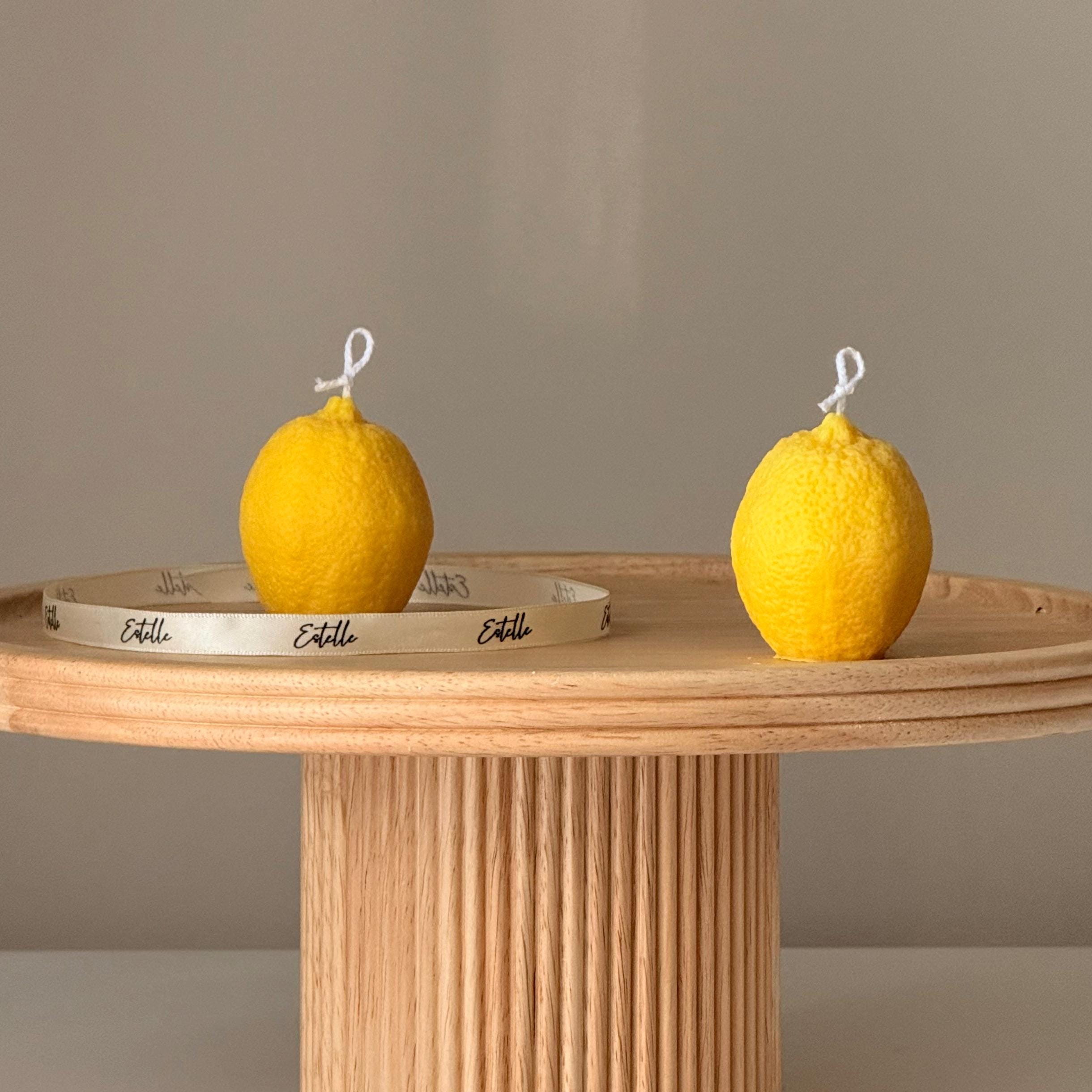 Two lemon-shaped candles on a wooden table with a plain background