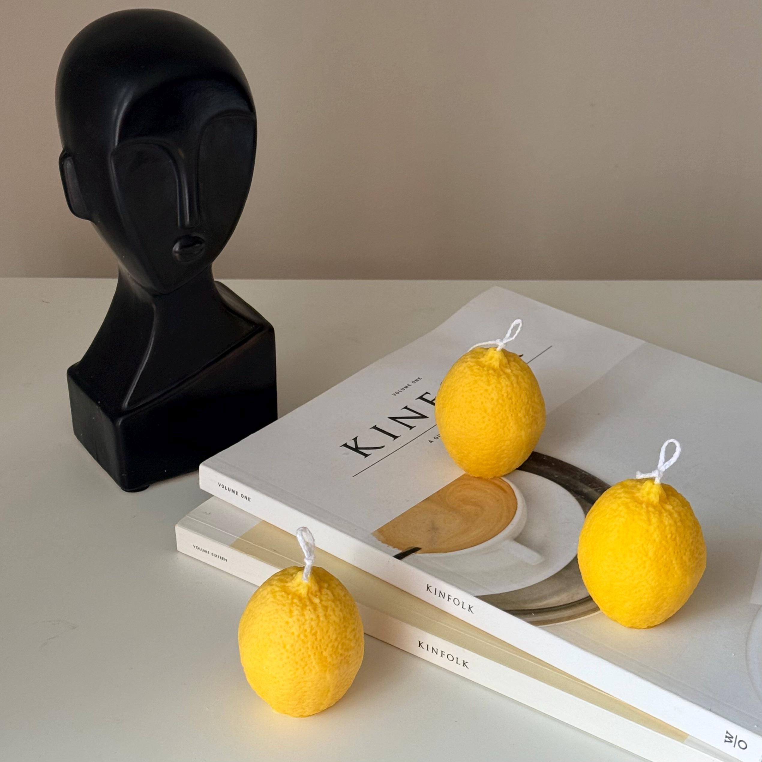 Yellow lemon-shaped candles on a stack of books with a black bust sculpture in the background.