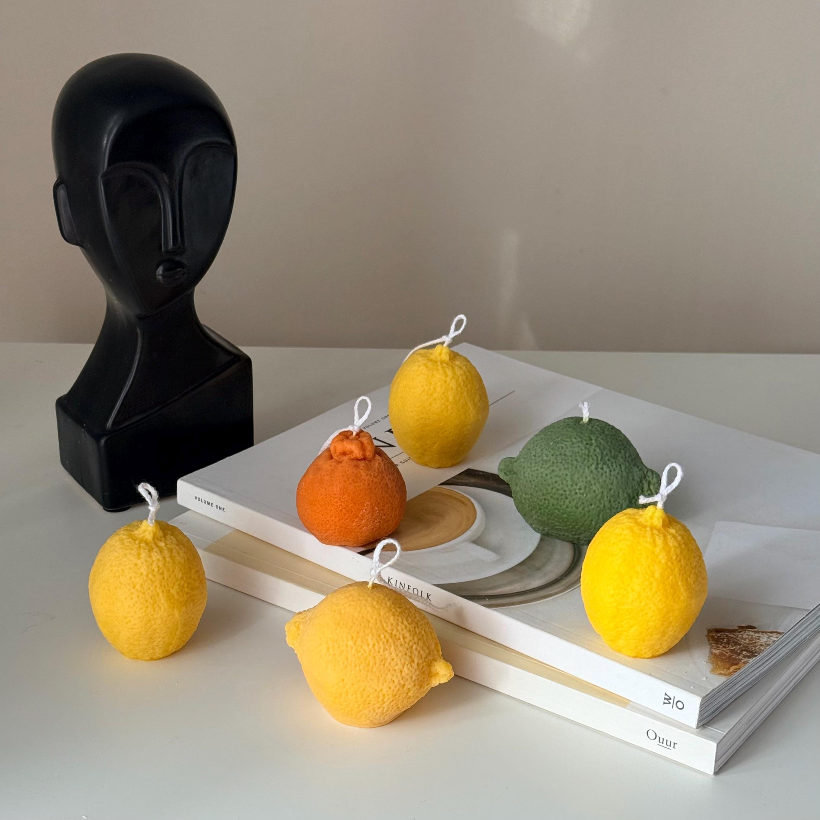Candle-shaped like lemons on books with a black sculpture in the background