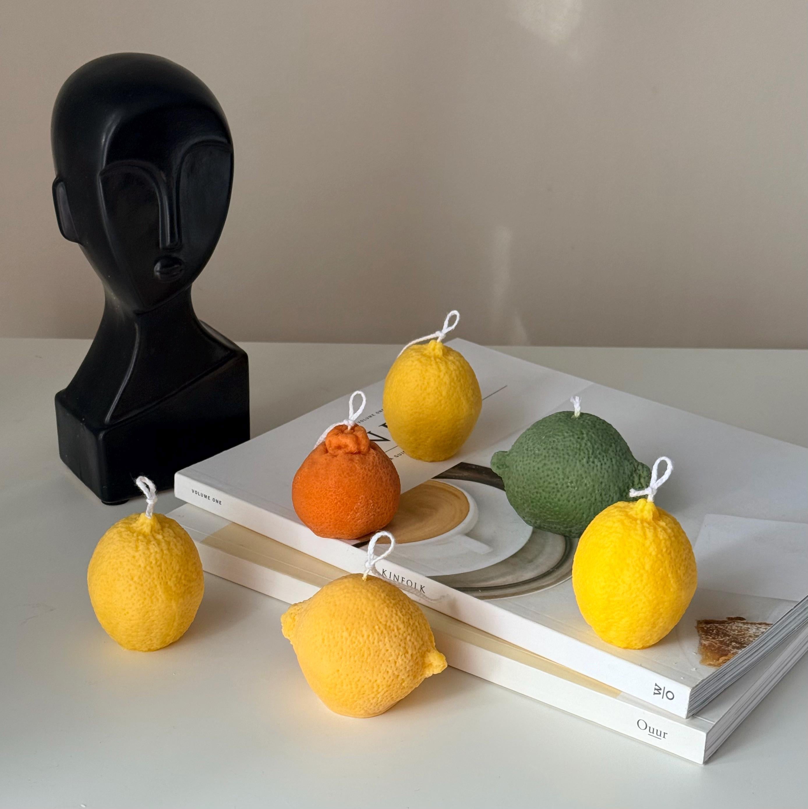 Candle-shaped like lemons on books with a black sculpture in the background