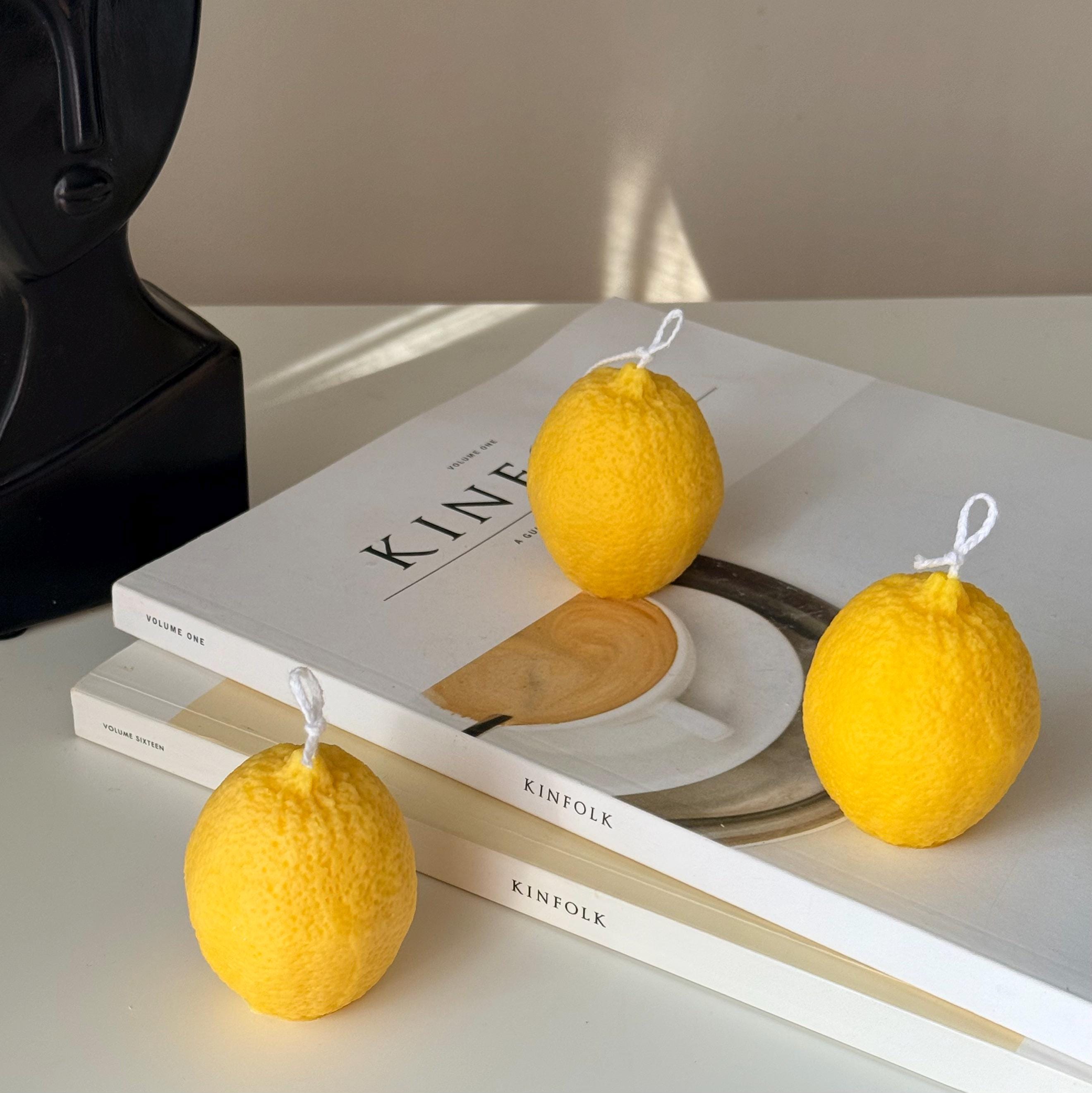 Three lemon-shaped candles on top of books with a neutral background