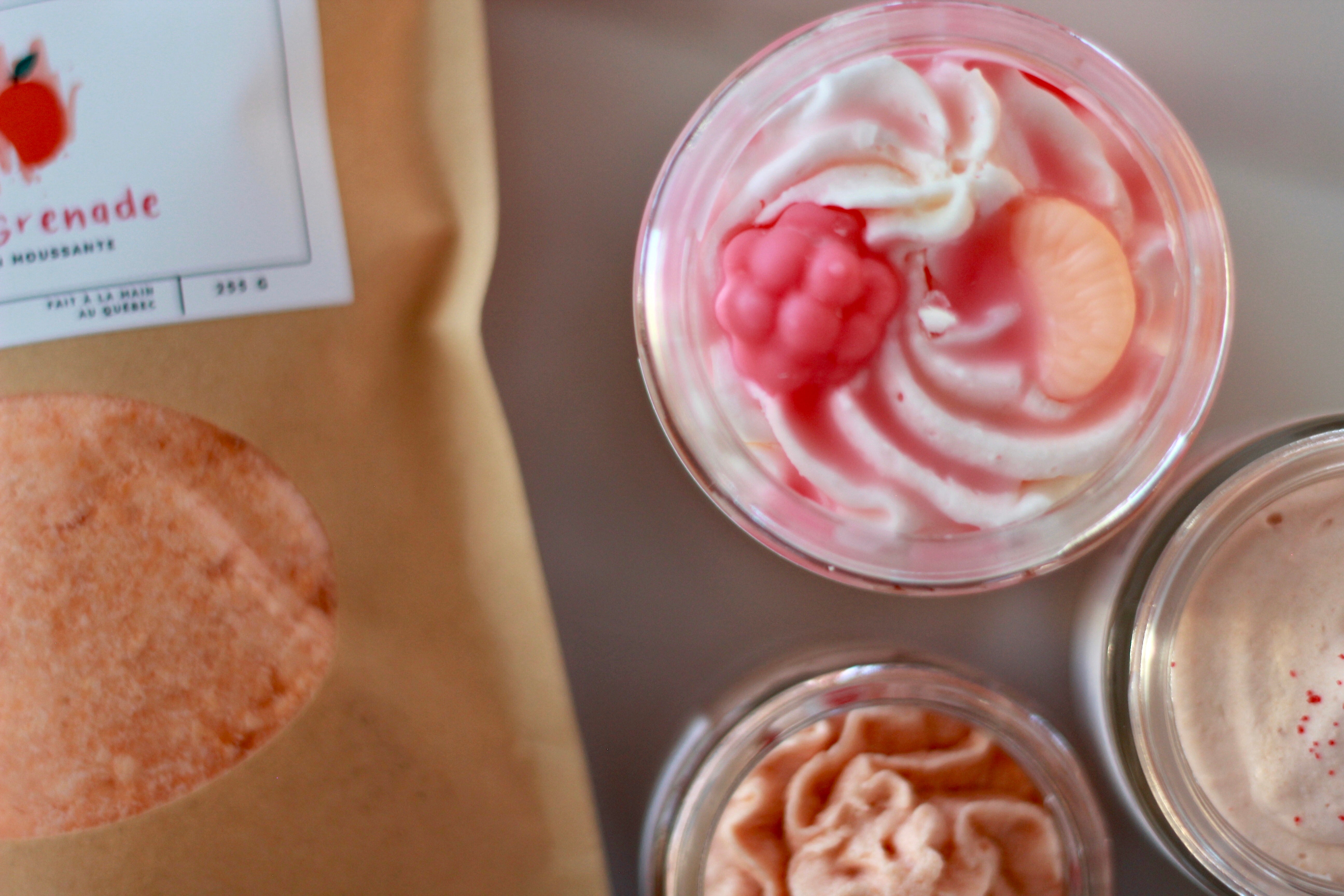 Assorted food items including a bag of 'Grenade' and containers with pink and white toppings on a metallic surface.
