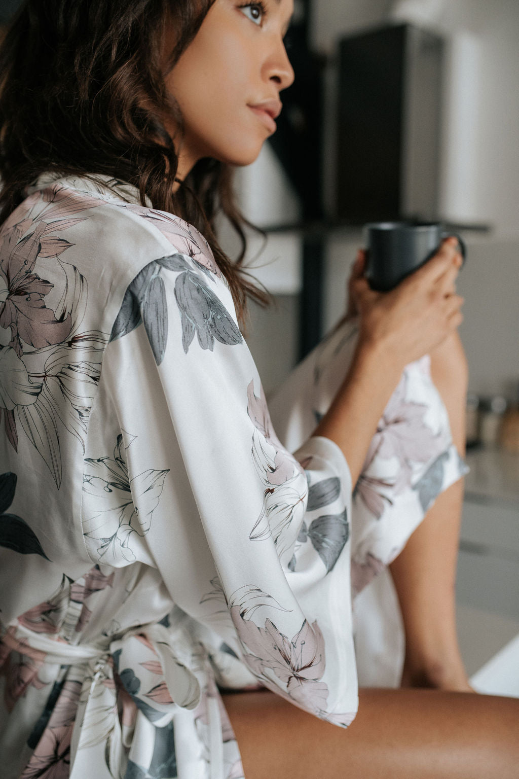 Woman in a floral robe holding a mug in a kitchen setting