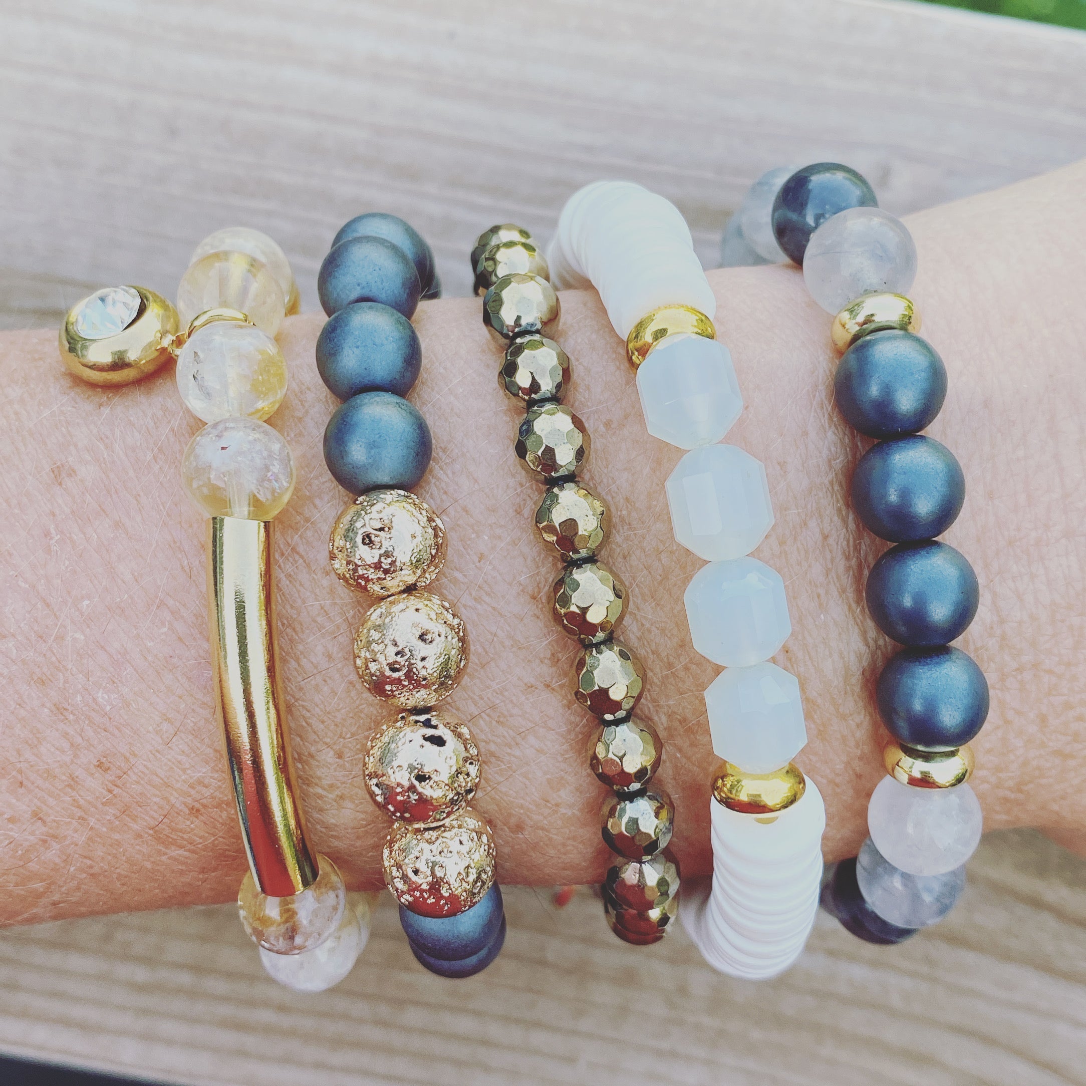Multiple beaded bracelets with blue, gold, and white beads on a wrist.