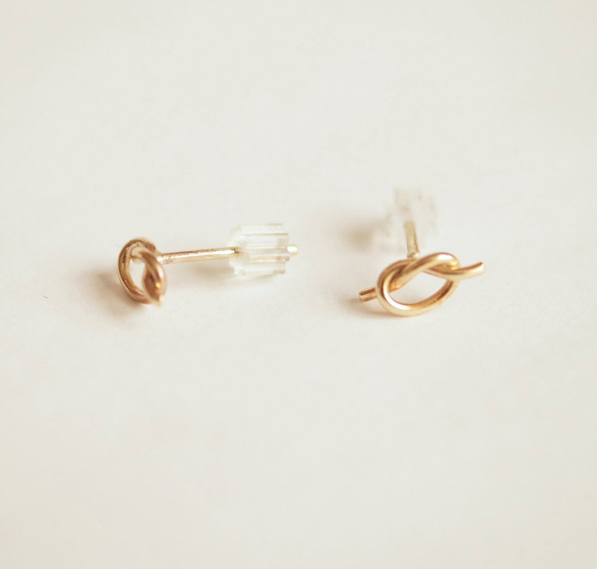Gold knot earrings on a light beige background