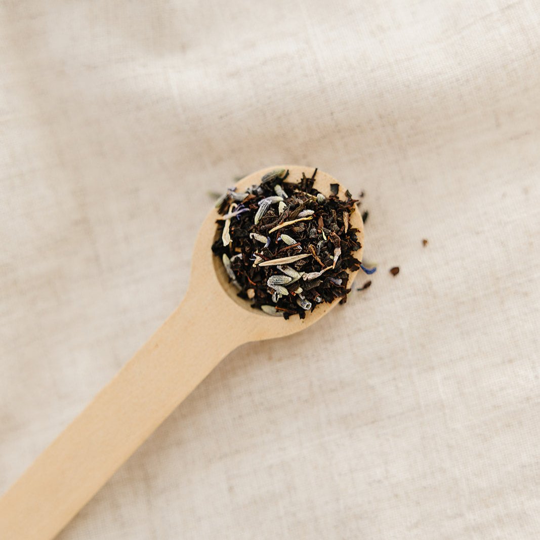 Wooden spoon filled with black tea leaves on a beige background