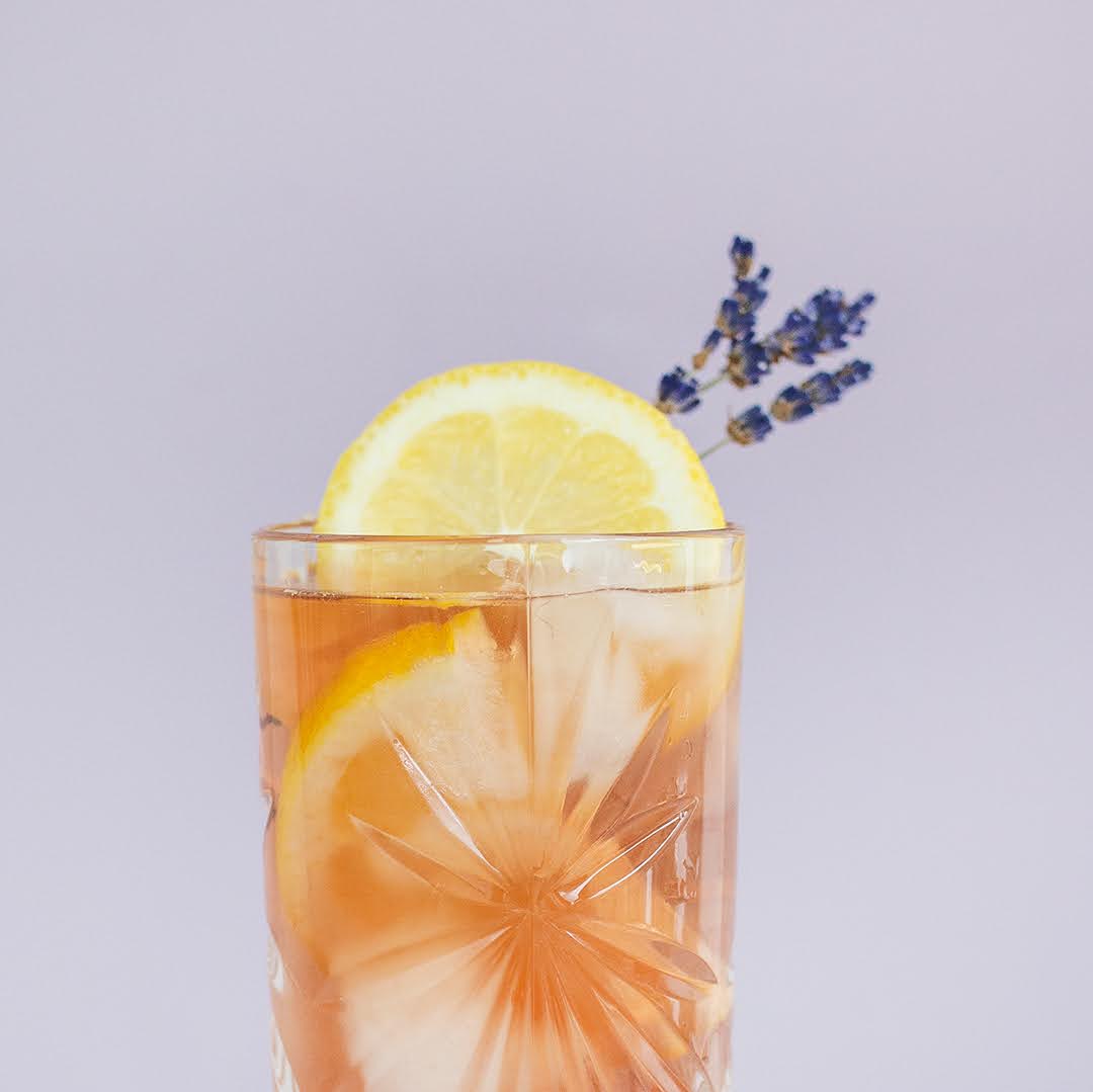 Glass of iced tea with lemon slices and lavender on a light purple background