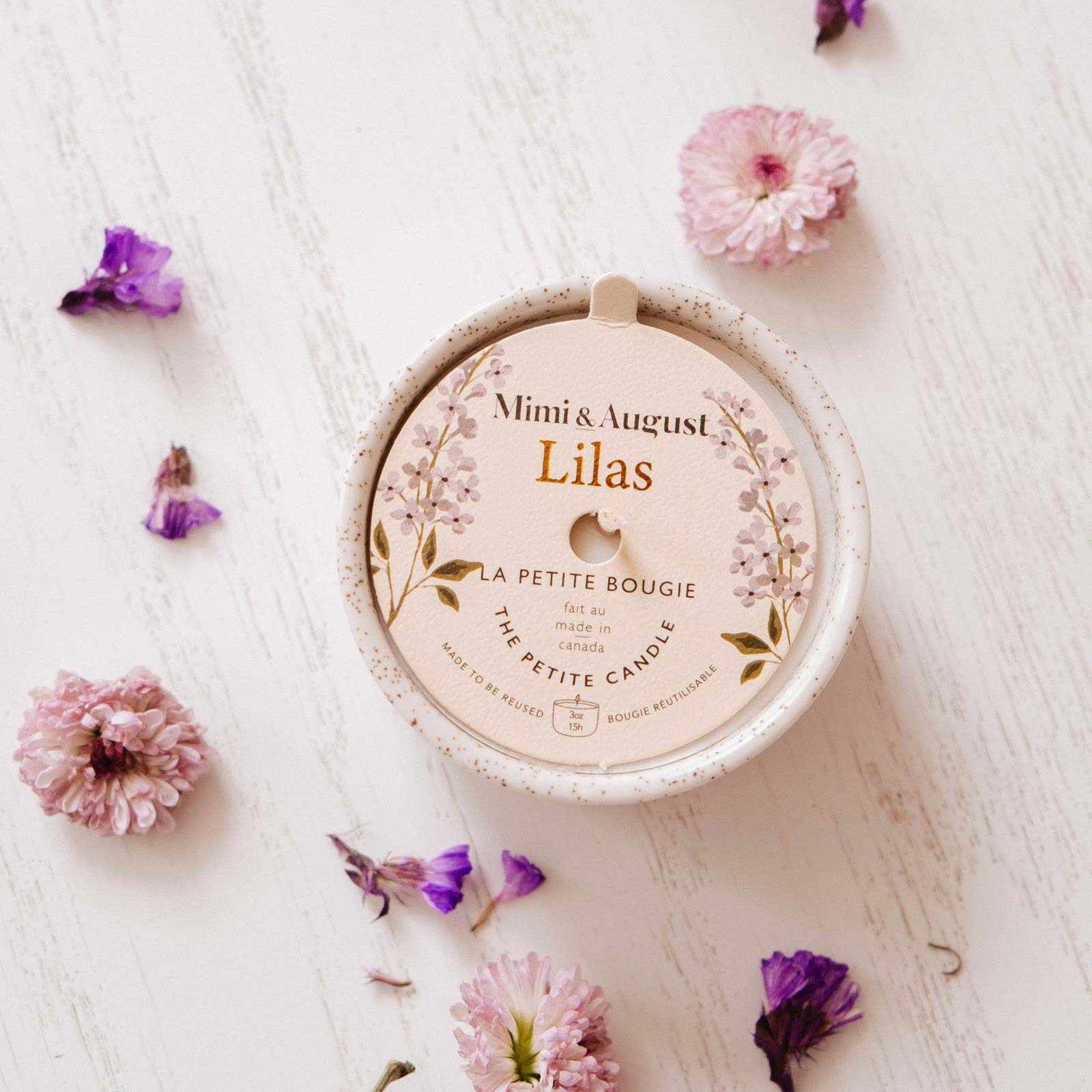 Mimi & August Lilas candle on a white surface with flowers around it mimi-and-august