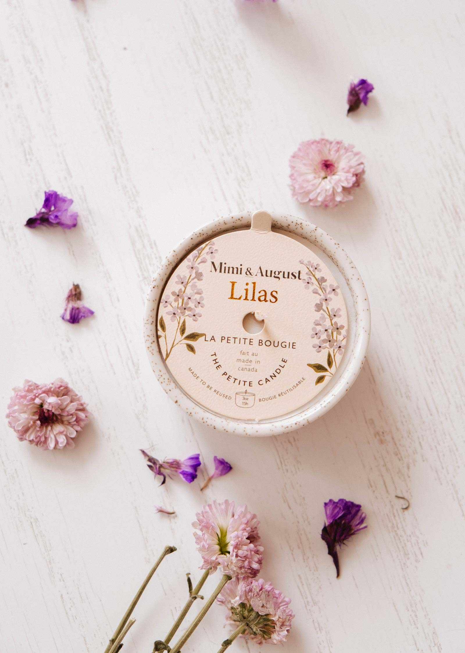 Mimi & August Lilas candle on a white surface with flowers around it mimi-and-august