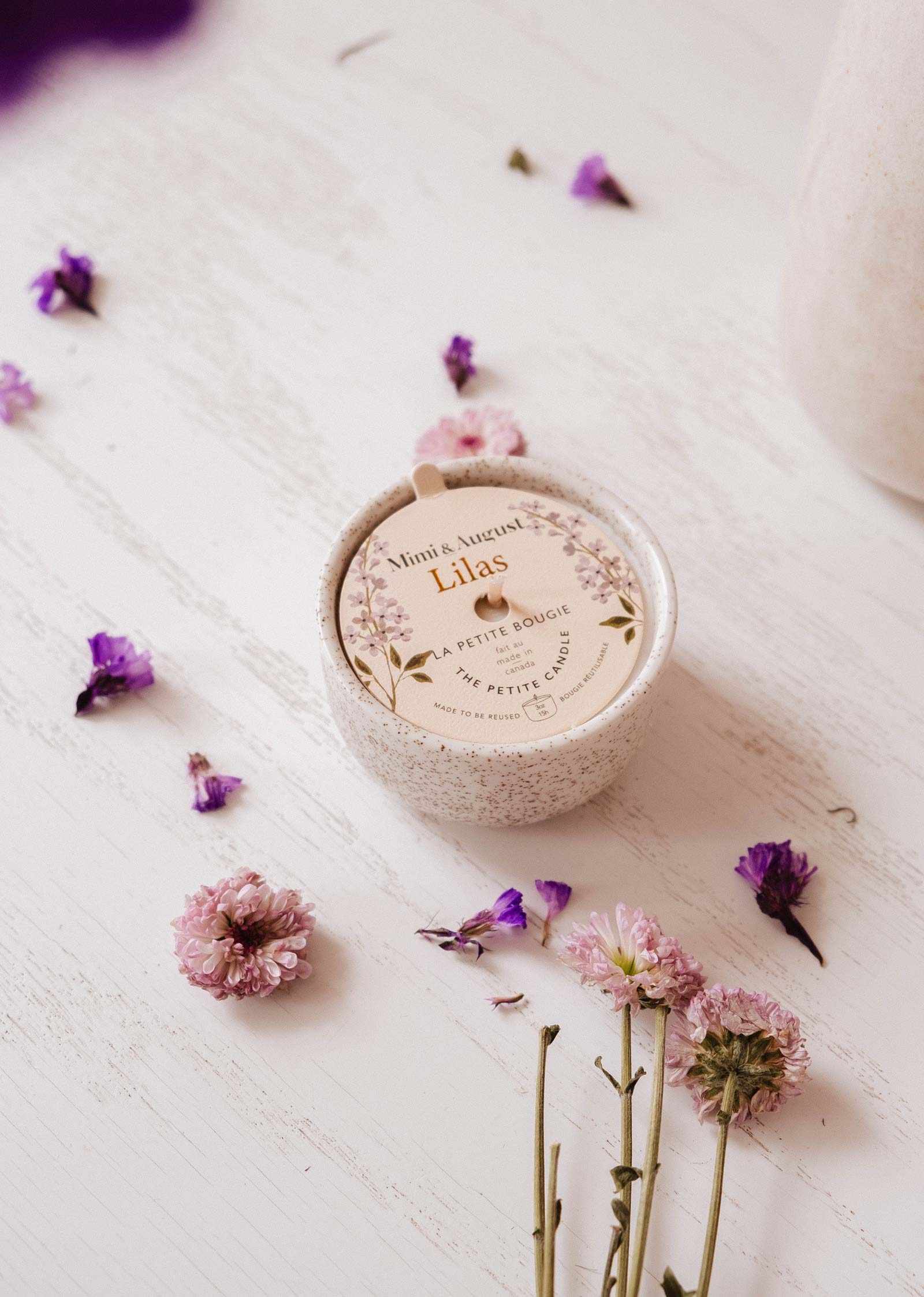 Round container labeled 'Lilas' with scattered flowers on a textured surface mimi-and-august