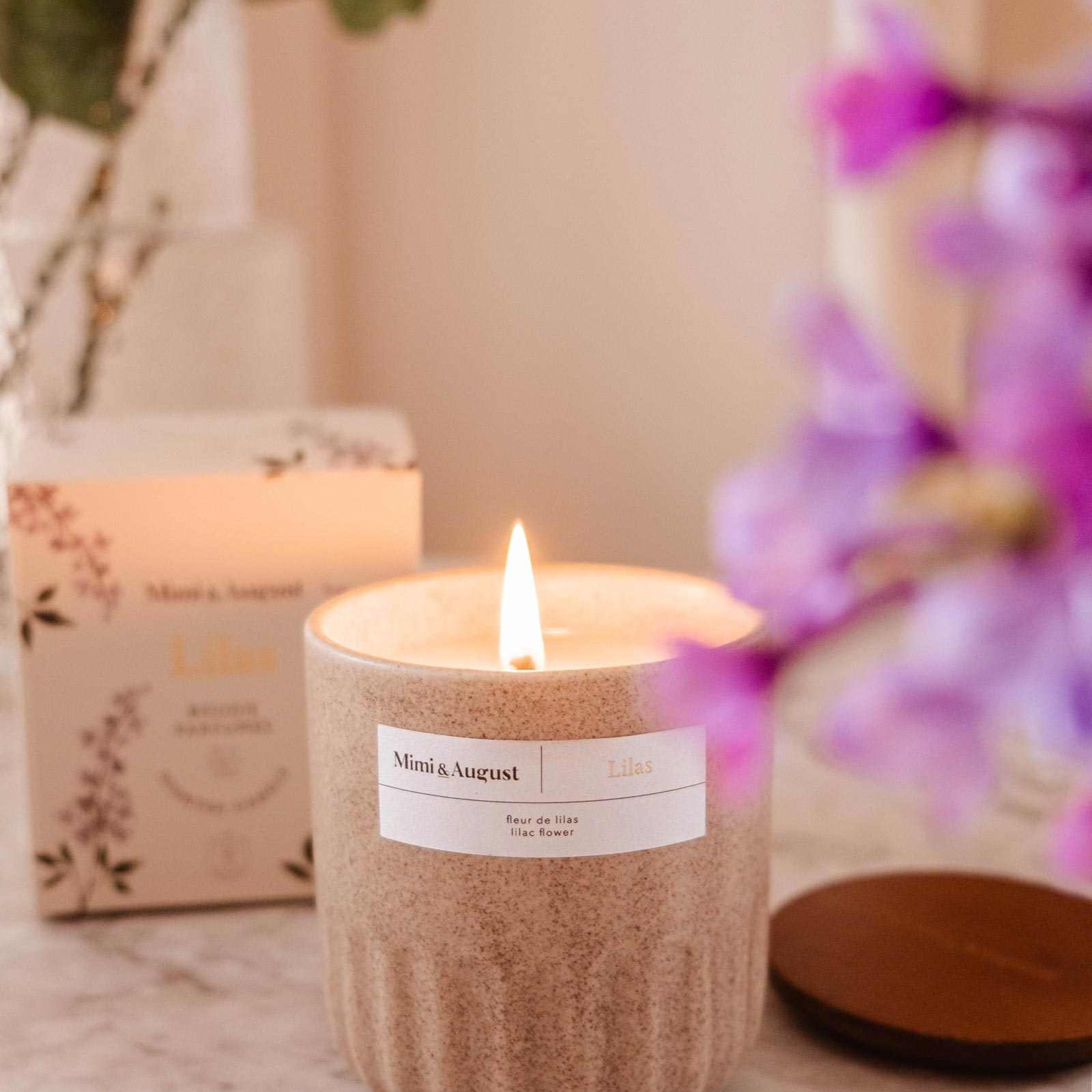 Candle with a label on a marble surface with flowers and packaging in the background mimi-and-august