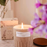 Candle with a label on a marble surface with flowers and packaging in the background mimi-and-august