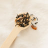 Wooden spoon filled with dried tea leaves on a light background of Bush Berry Organic Masala Chai Tea 