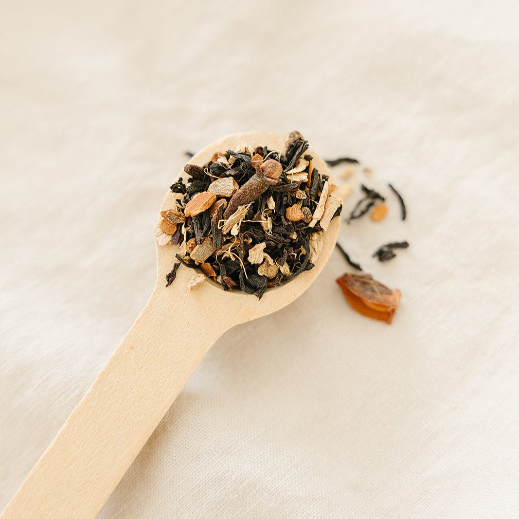 Wooden spoon filled with dried tea leaves on a light background of Bush Berry Organic Masala Chai Tea 