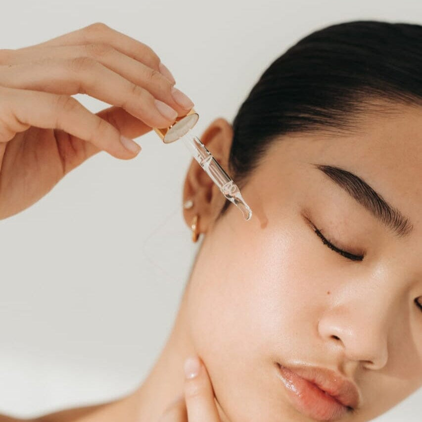 Person applying a skincare product to a woman's face with a neutral background