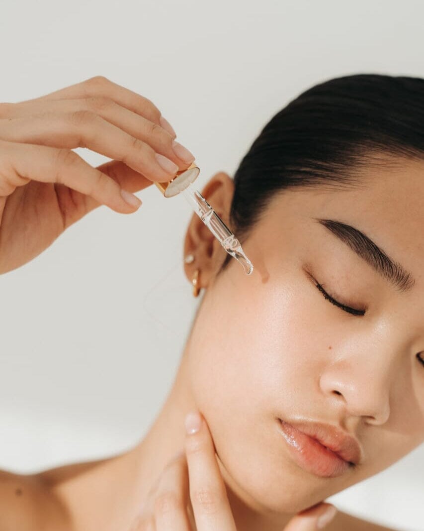 Person applying a skincare product to a woman's face with a neutral background