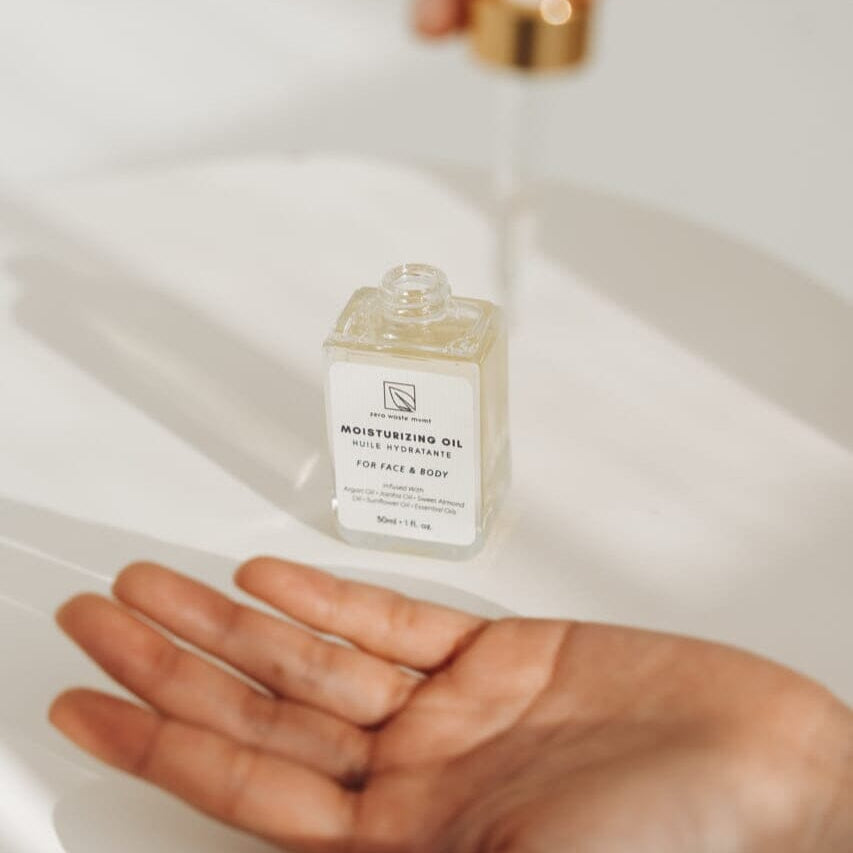 Small bottle of moisturizing oil held over a hand on a white background