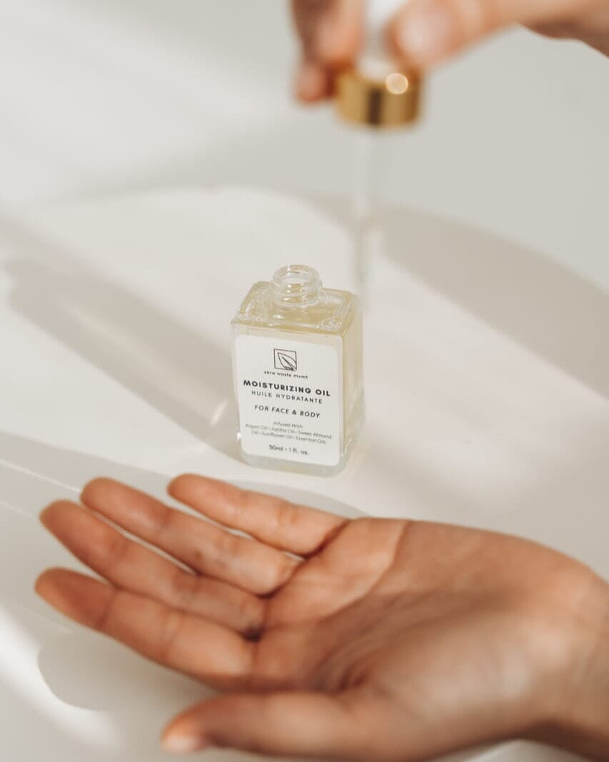 Small bottle of moisturizing oil held over a hand on a white background