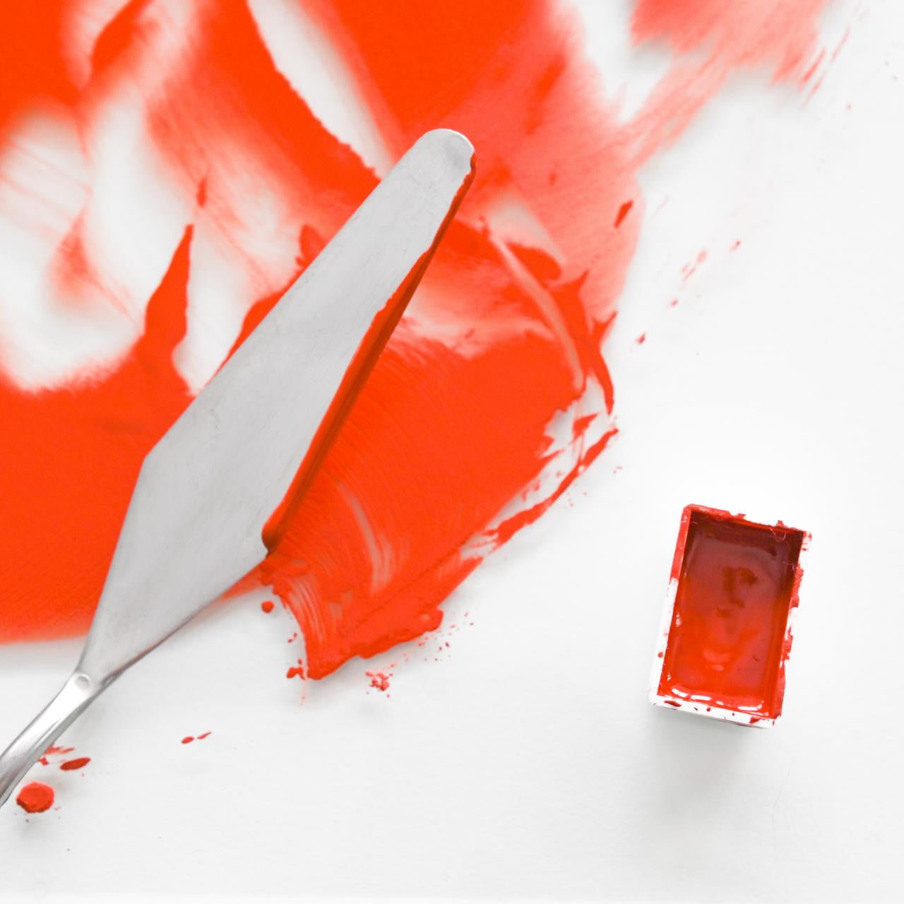 Red paint splatter on a white surface with a knife and red paint container.