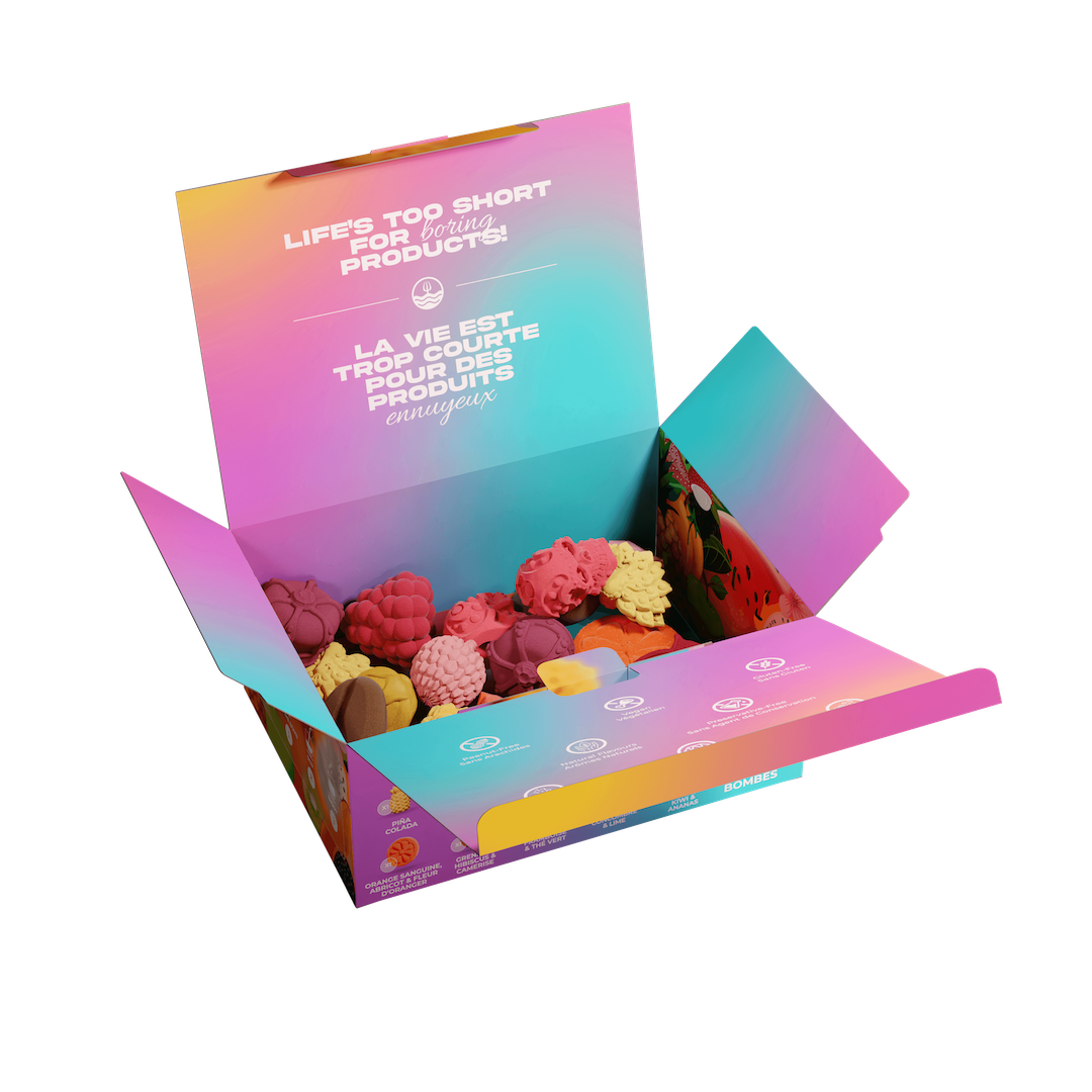 An open gift box filled with colorful novelty items, shown on a plain white background. The box has a pink, purple, and blue gradient design with French text on the inside lid.