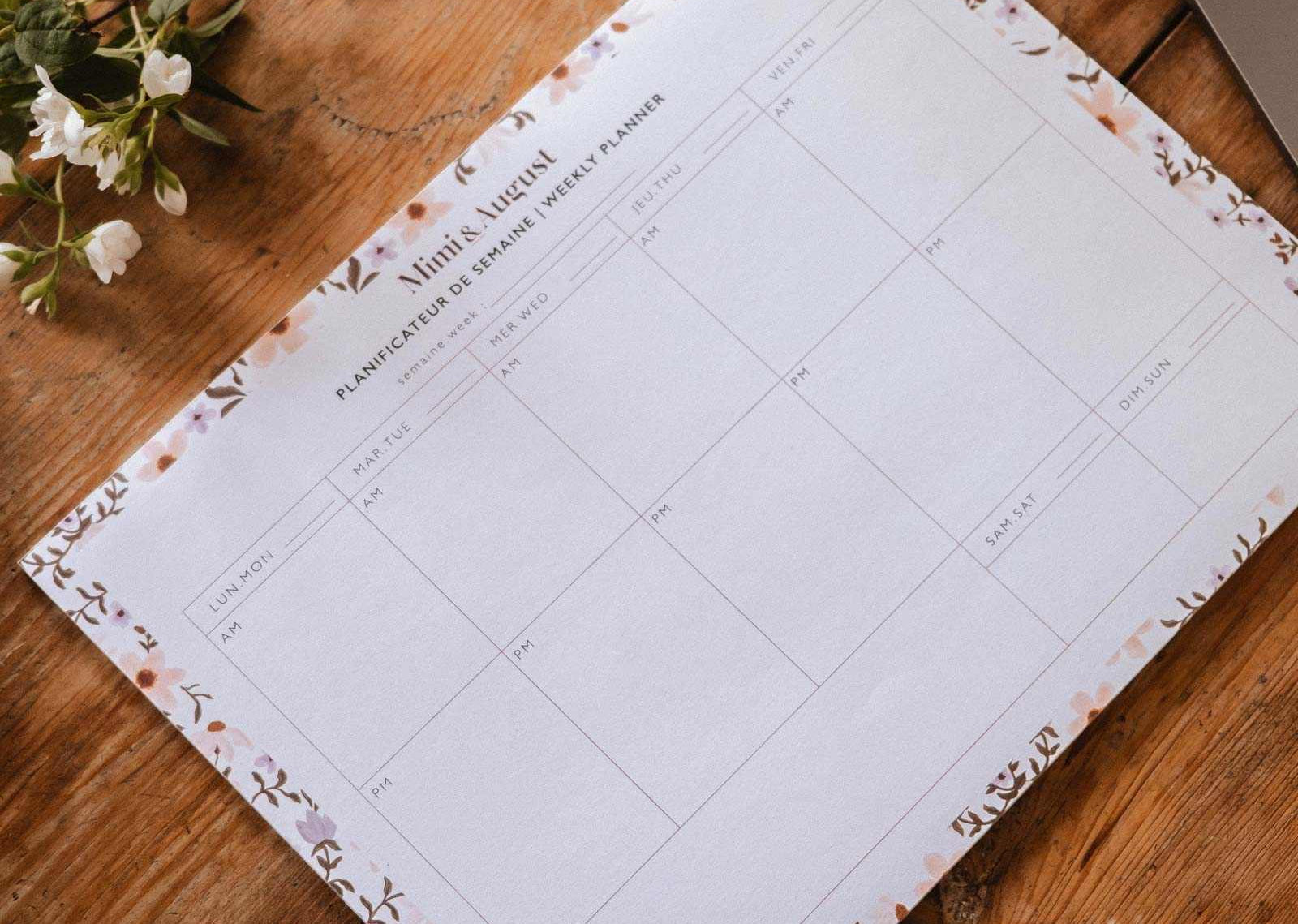 Floral planner sheet on a wooden desk with a pen and laptop.