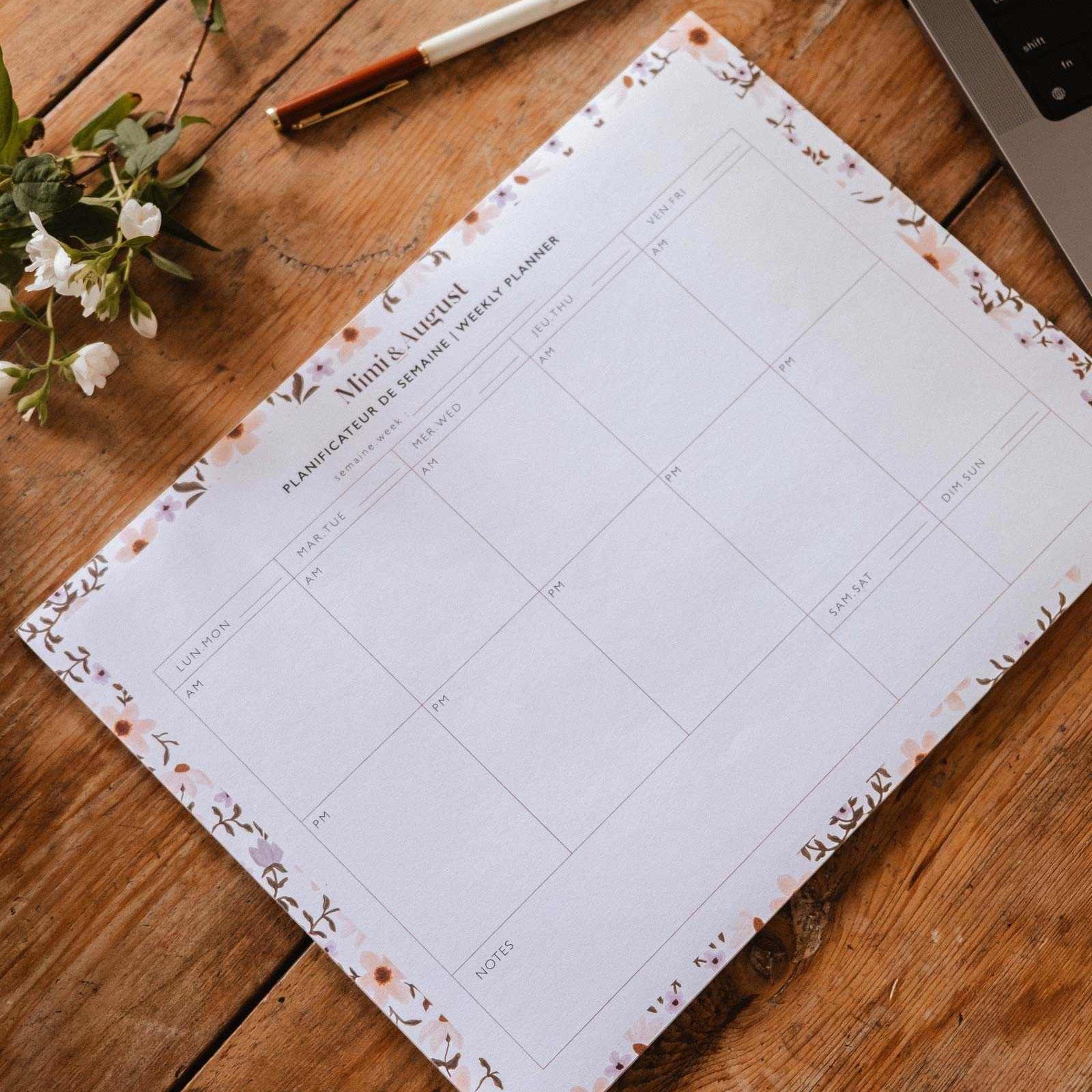 Floral planner sheet on a wooden desk with a pen and laptop.