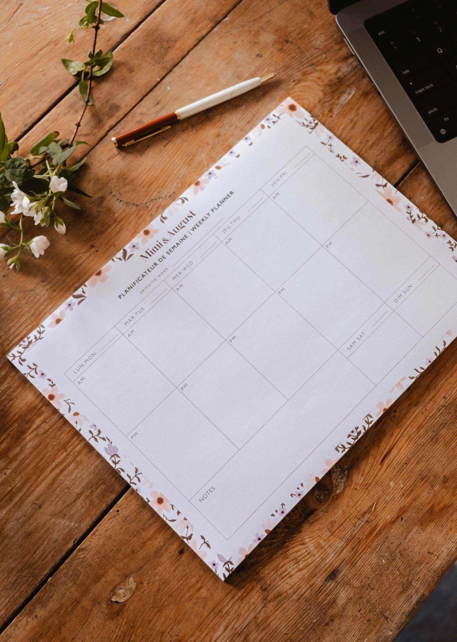 Floral planner sheet on a wooden desk with a pen and laptop.