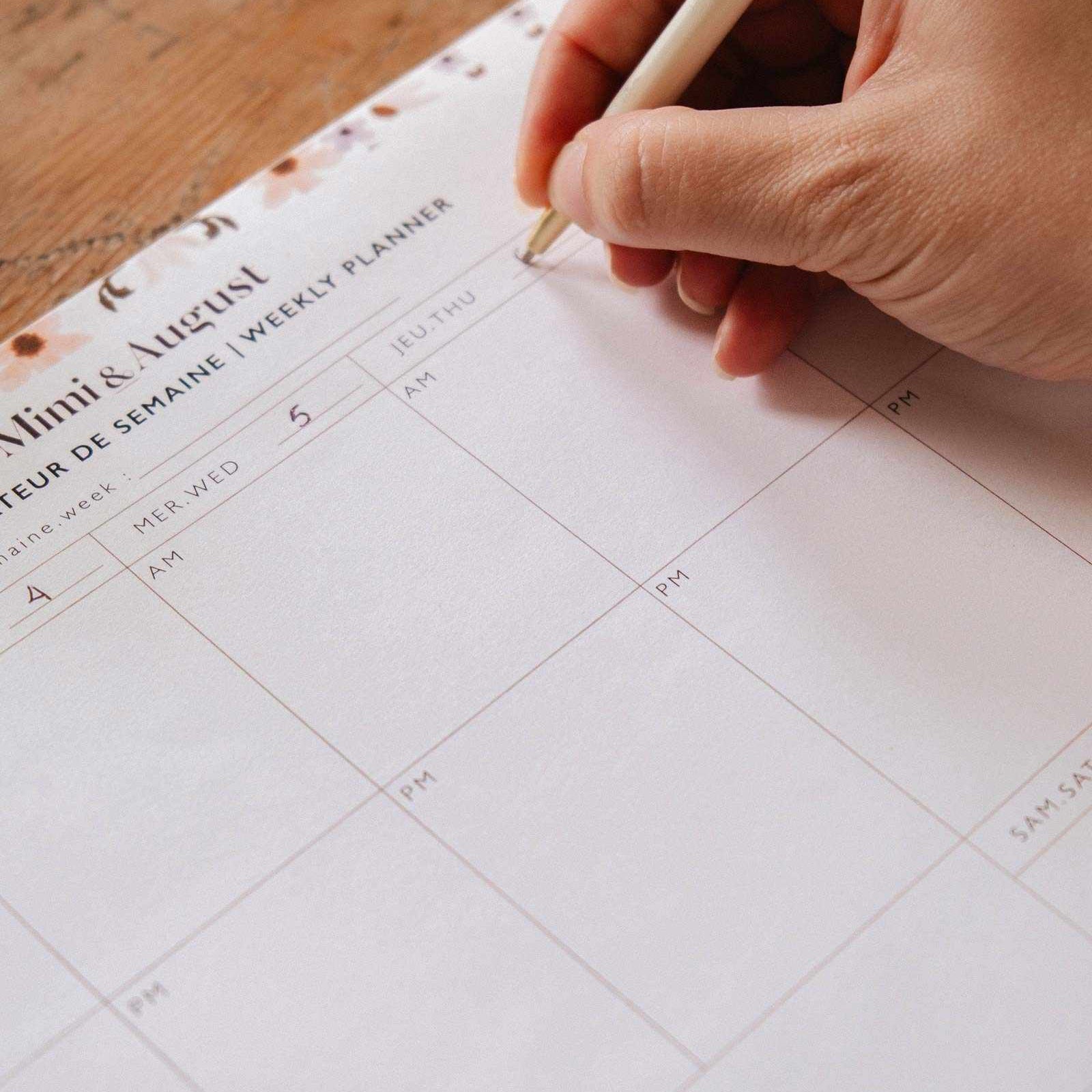 Hand holding a pen over a weekly planner on a wooden surface