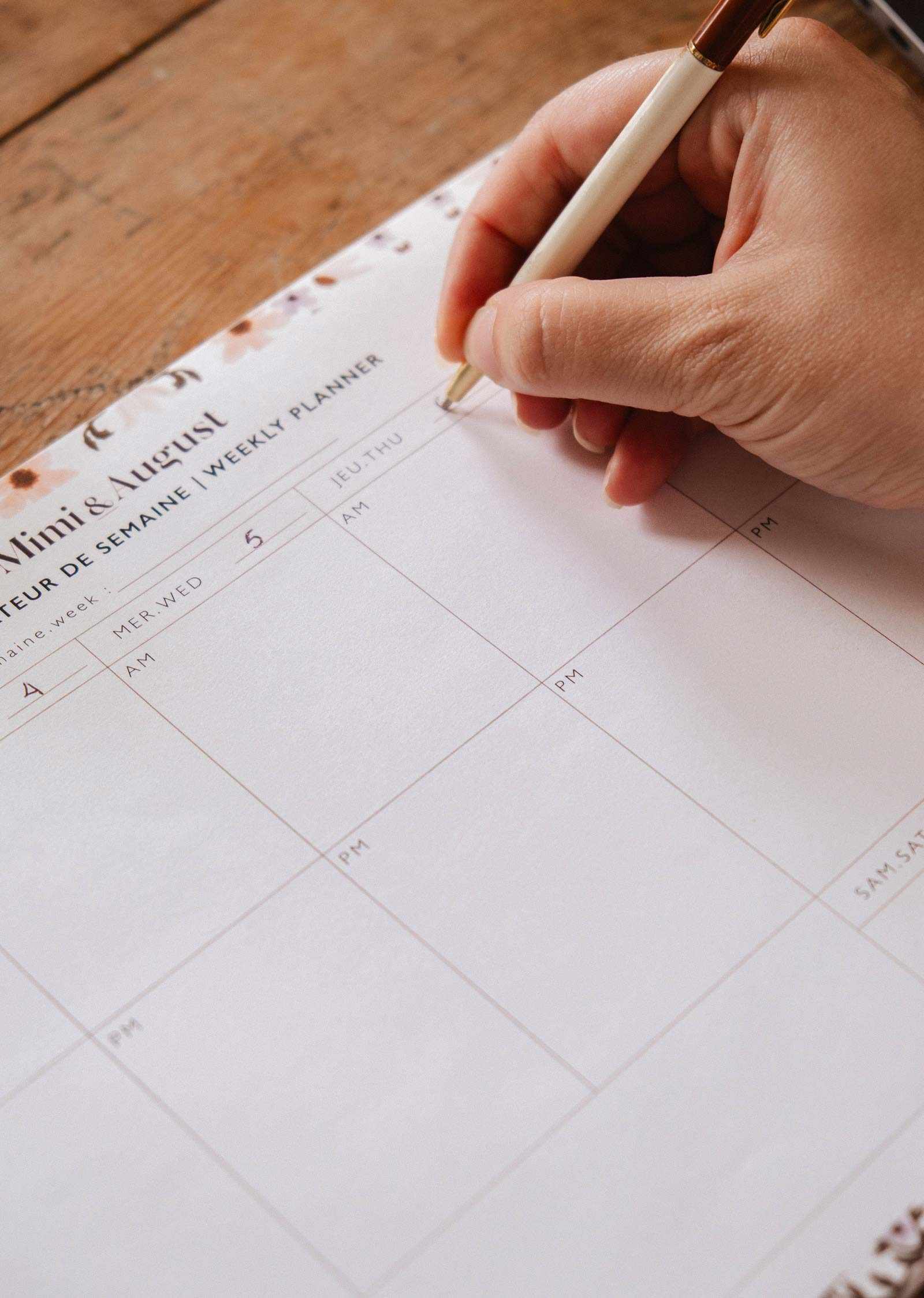 Hand holding a pen over a weekly planner on a wooden surface