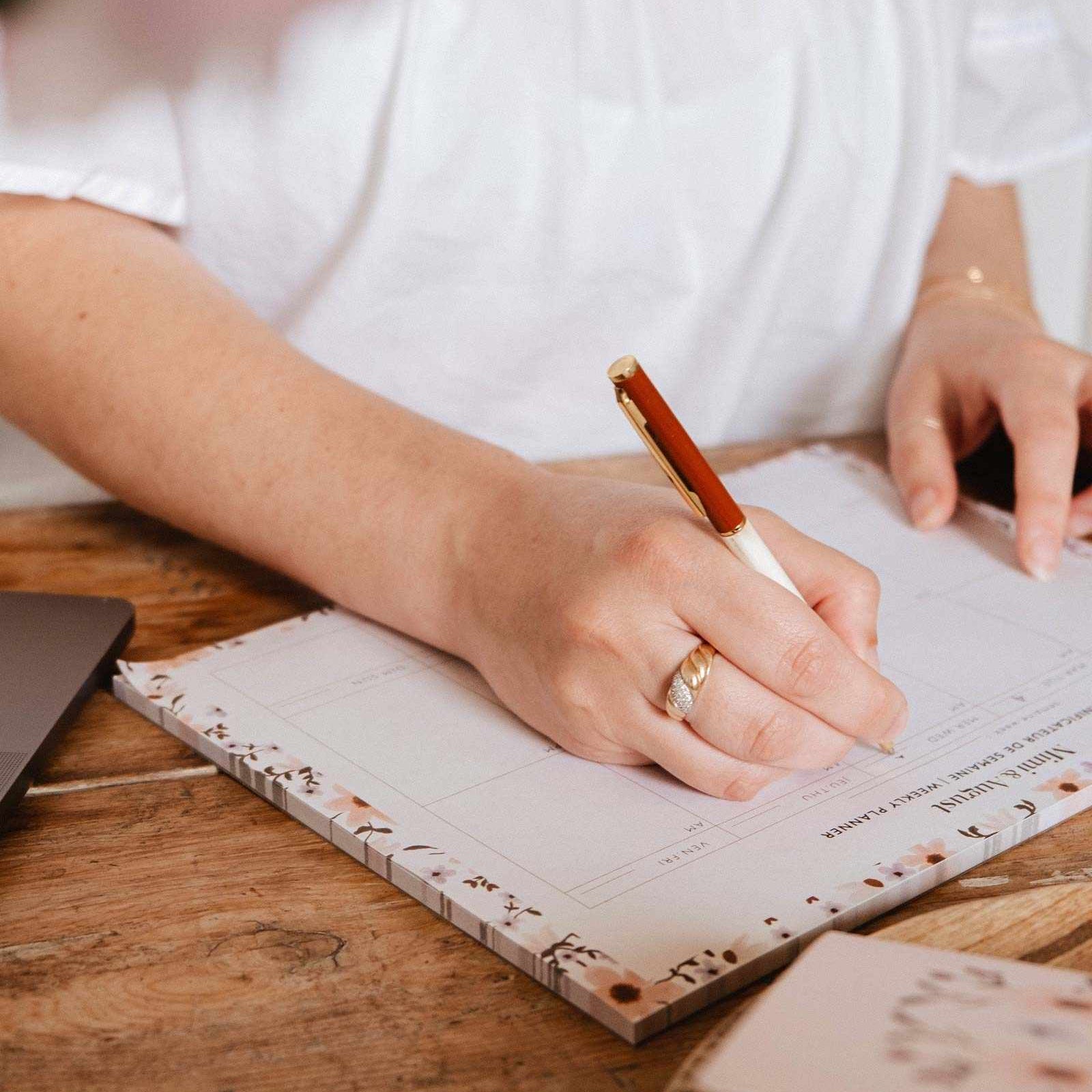 Person writing in a notebook with a pen on a wooden table