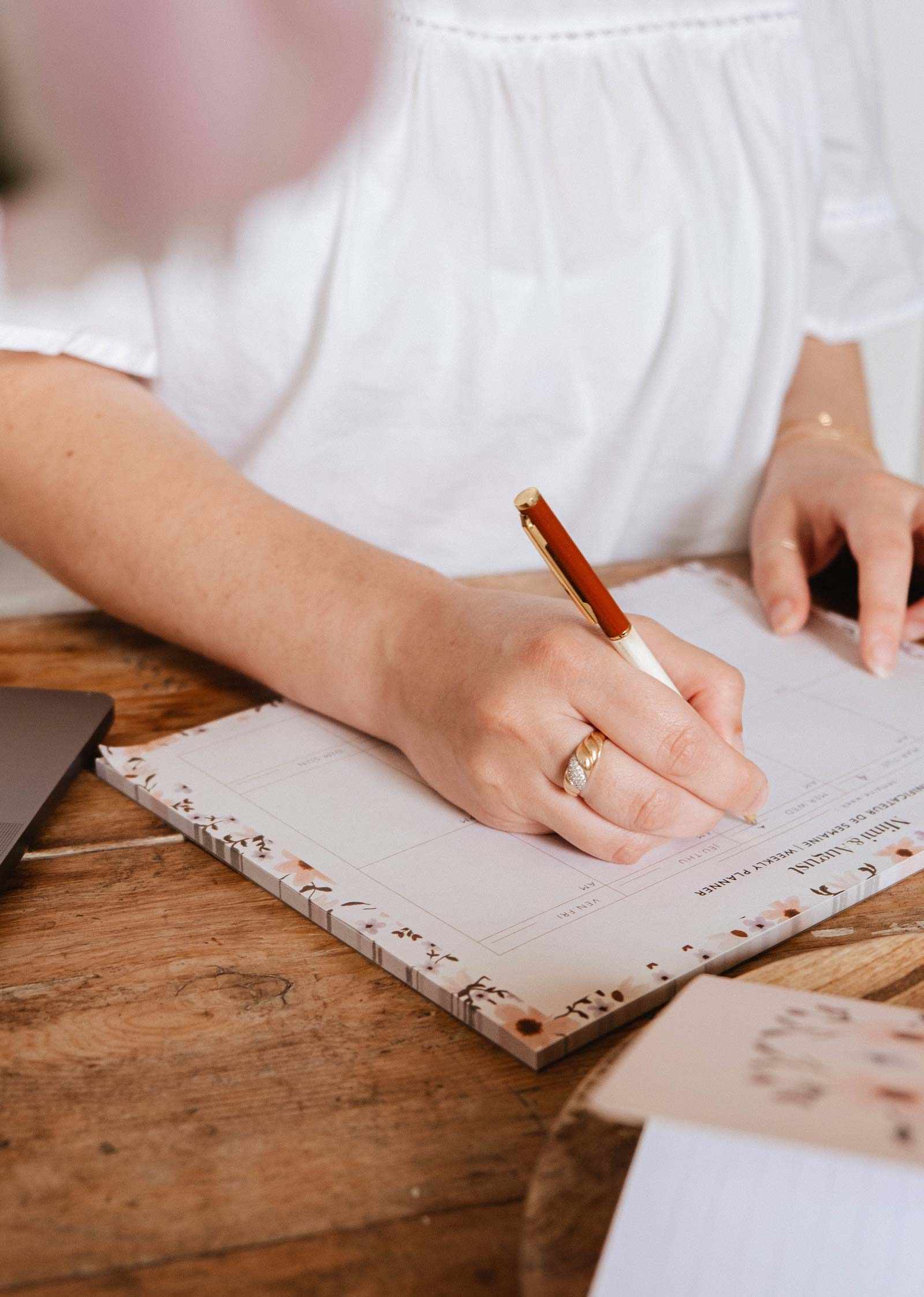 Person writing in a notebook with a pen on a wooden table