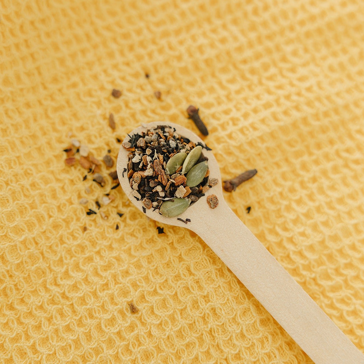 Wooden spoon with Organic Pumpkin Spice Tea dried herbs and seeds on a textured yellow background