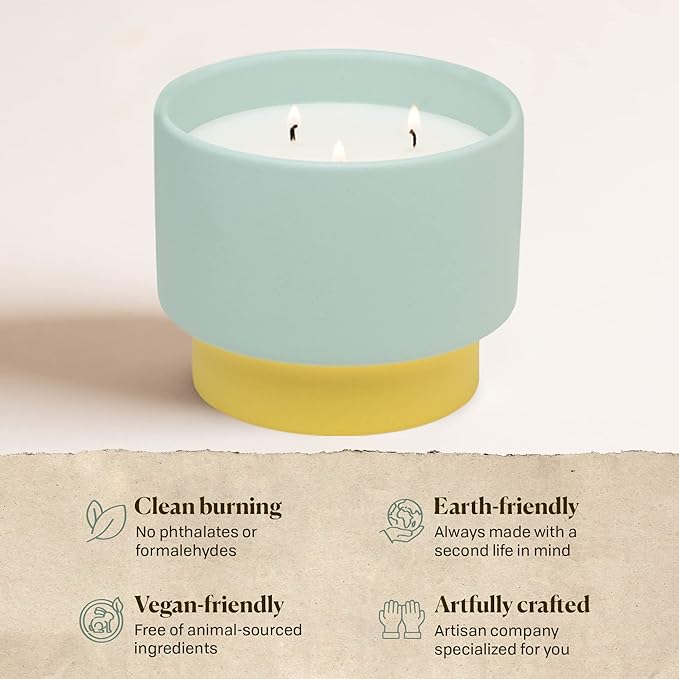 Candle in a light blue holder with yellow base on a beige background, featuring text about product attributes.