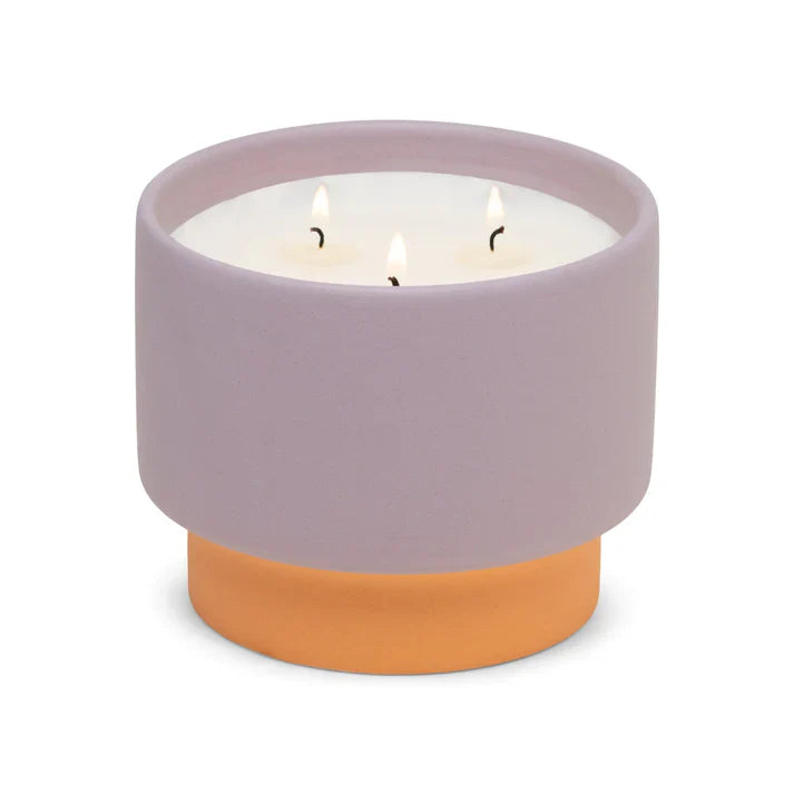 Candle in a purple container with a terracotta base on a white background