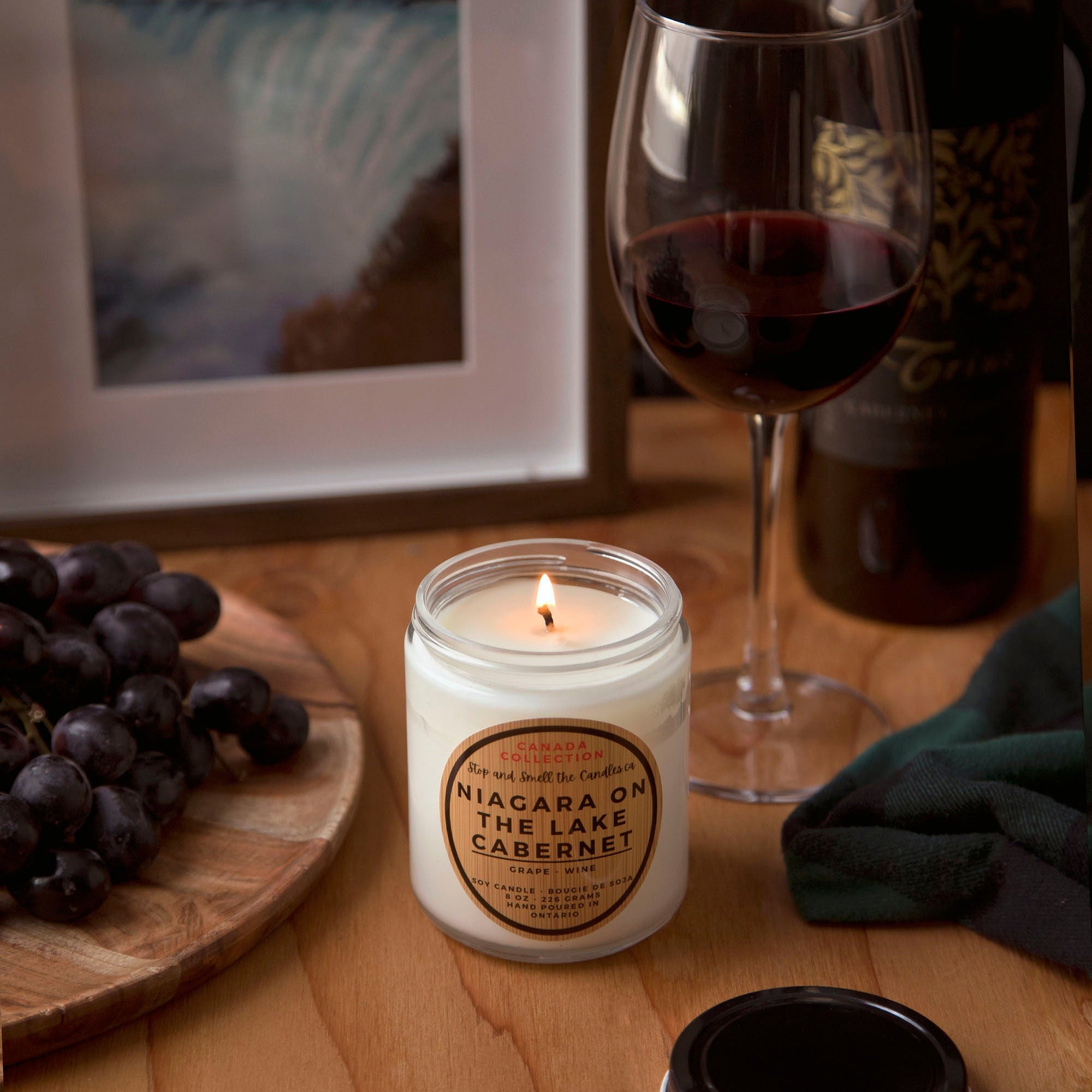 Candle labeled 'Niagara On The Lake Cabernet' next to a glass of red wine on a wooden table.