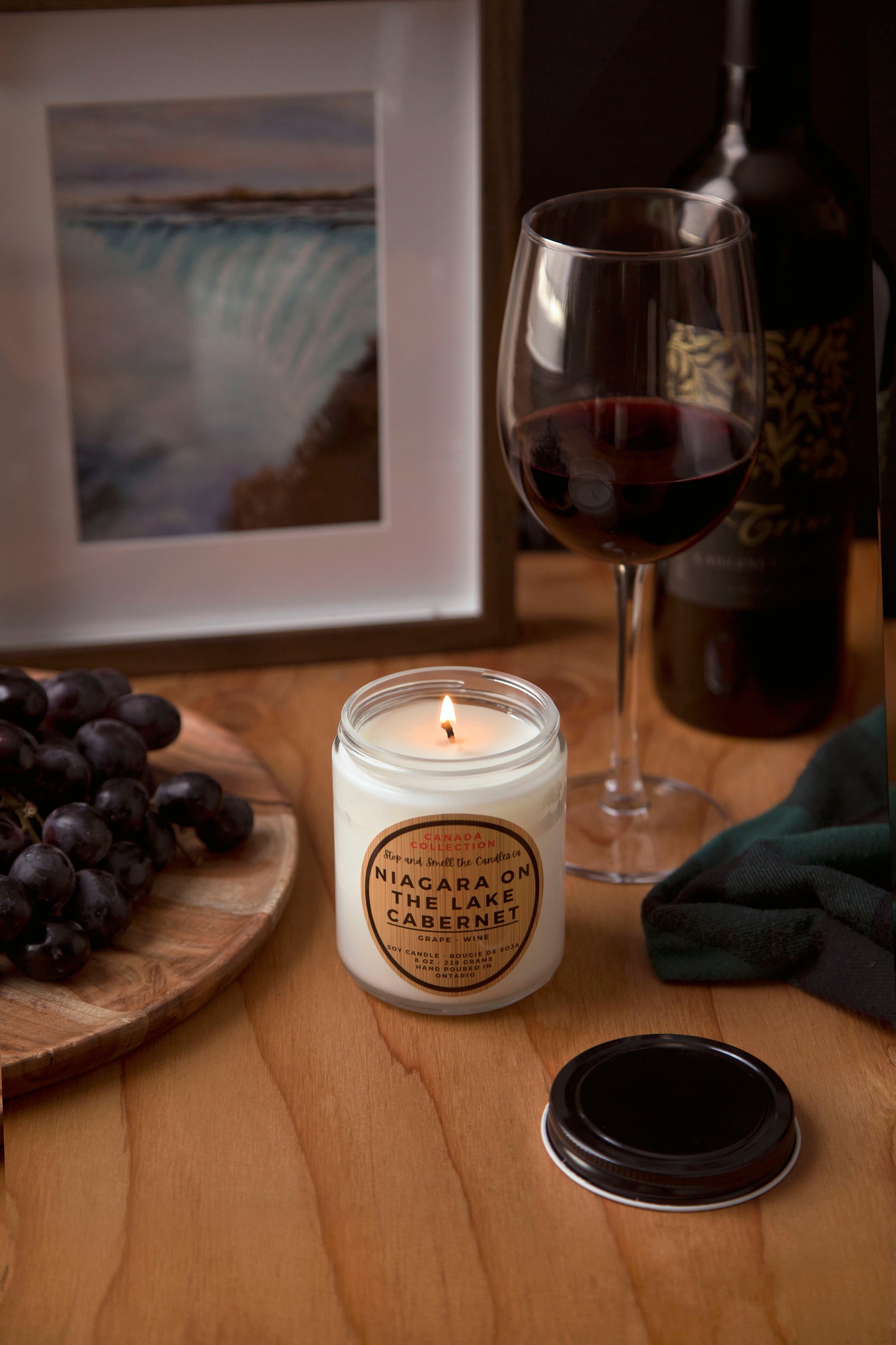 Candle labeled 'Niagara On The Lake Cabernet' next to a glass of red wine on a wooden table.